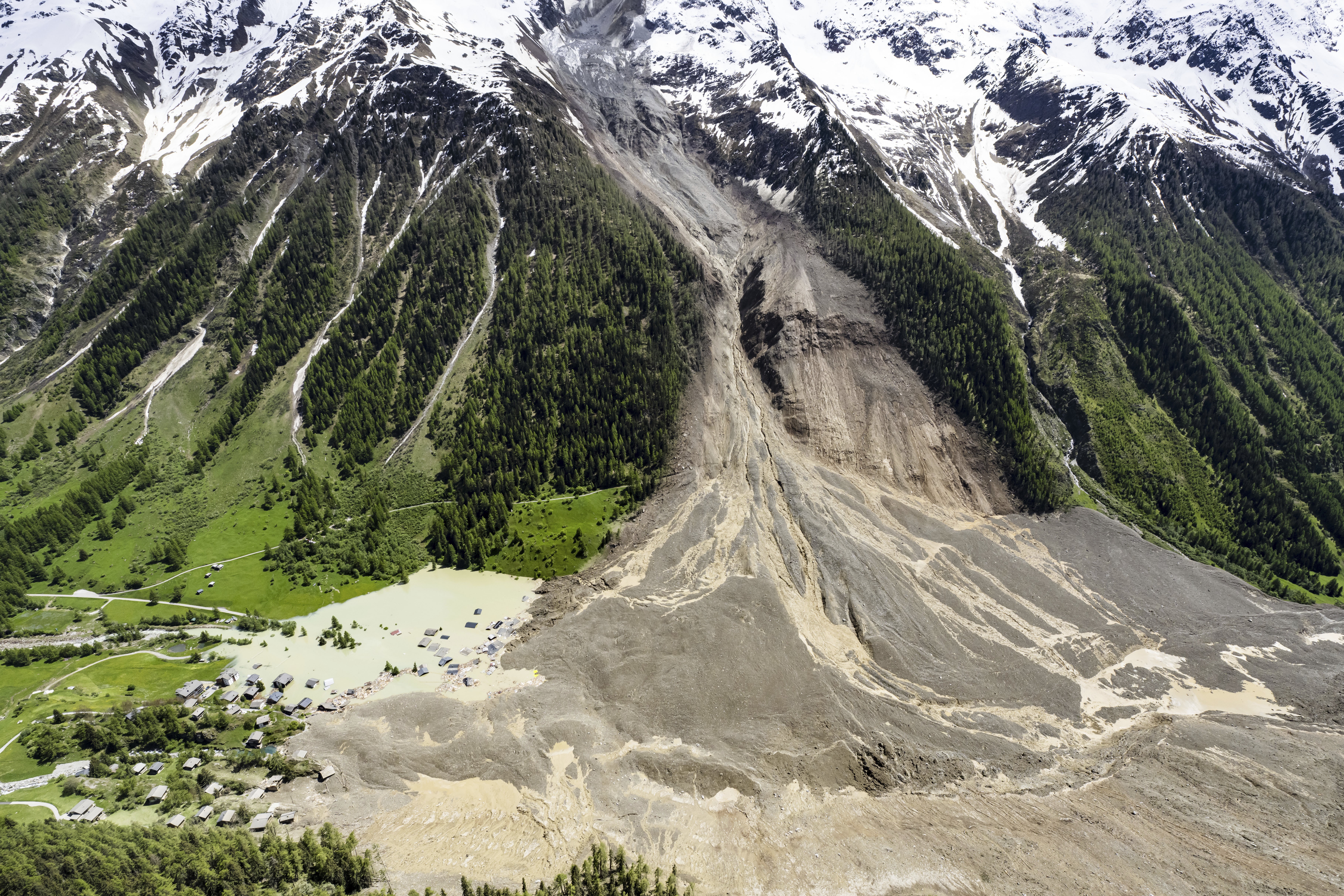 An aerial view of the side of a mountain valley, scarred by a recent landslide, covering much of a village below.