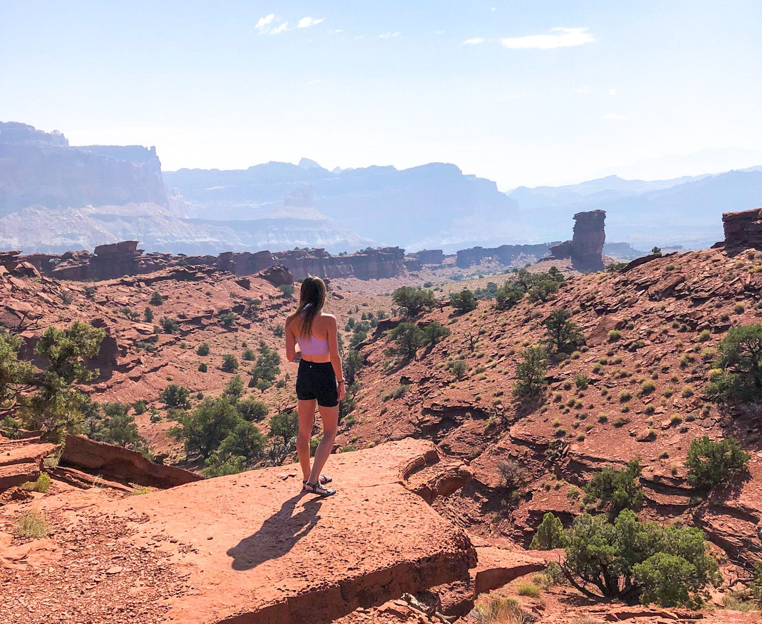 Emily, wearing a purple crop top and shorts, looks out at the rock formations at Capitol Reef National Park.