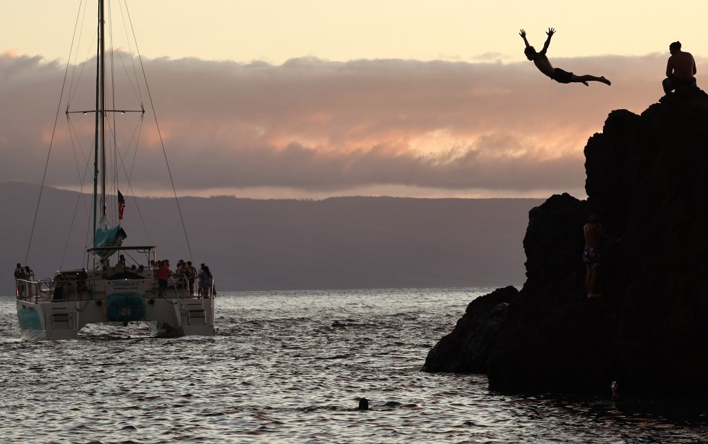 Person diving off rocks at Kaanapali Beach, Hawaii, as a tourist boat passes by
