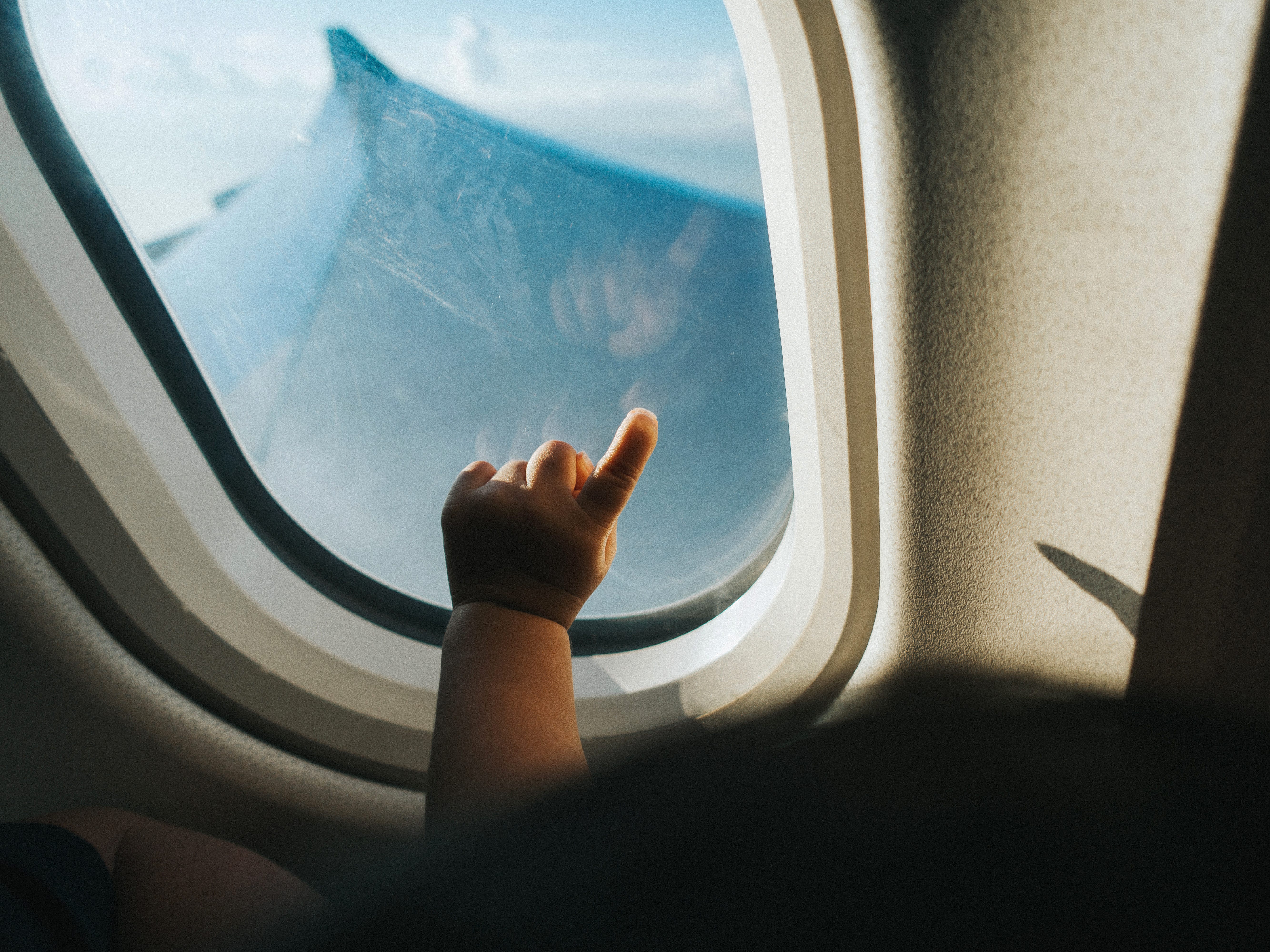 A toddler's hand points against the window of an airplane.