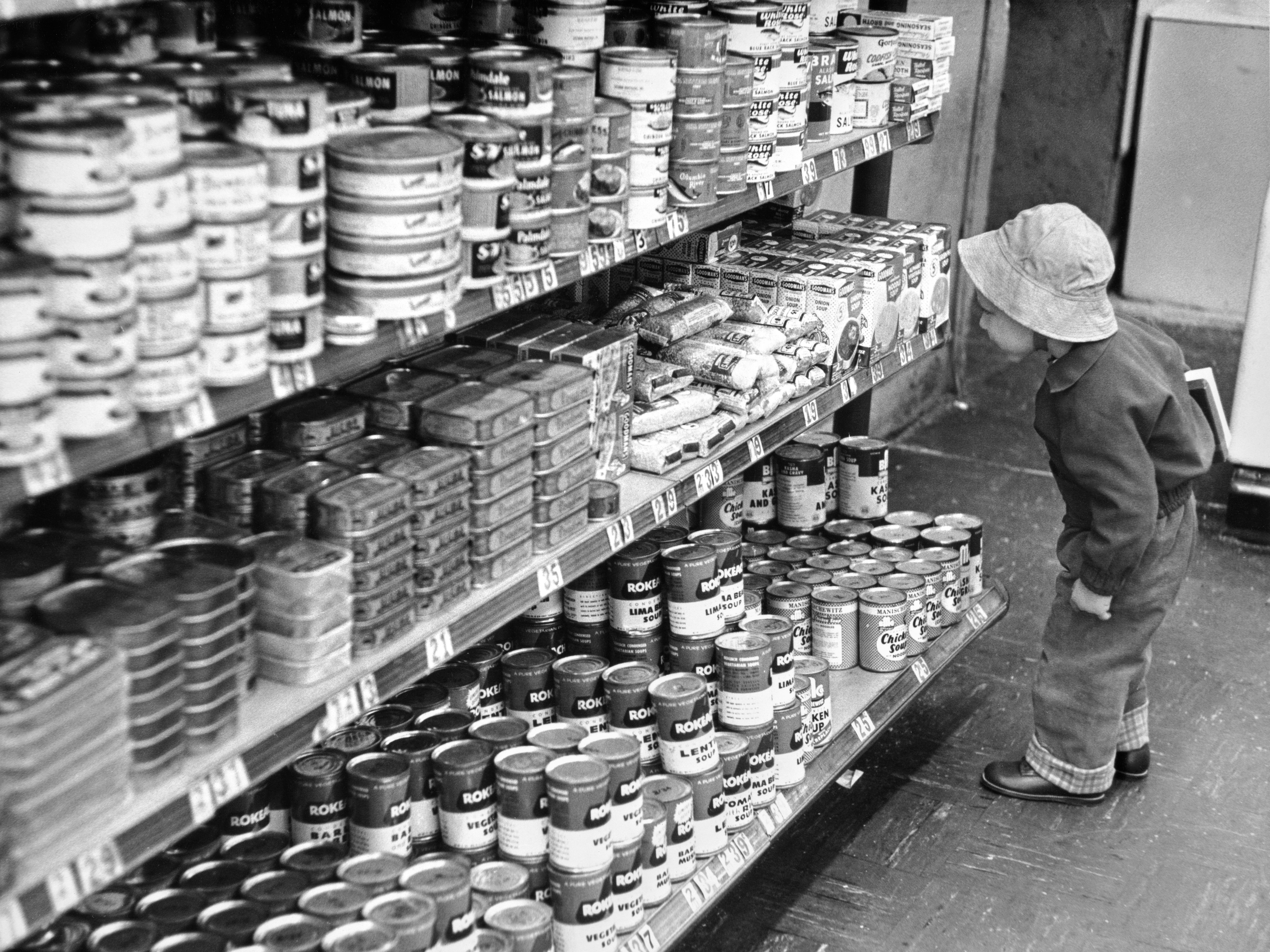 A child in a bucket hat looks at grocery store items on a shelf