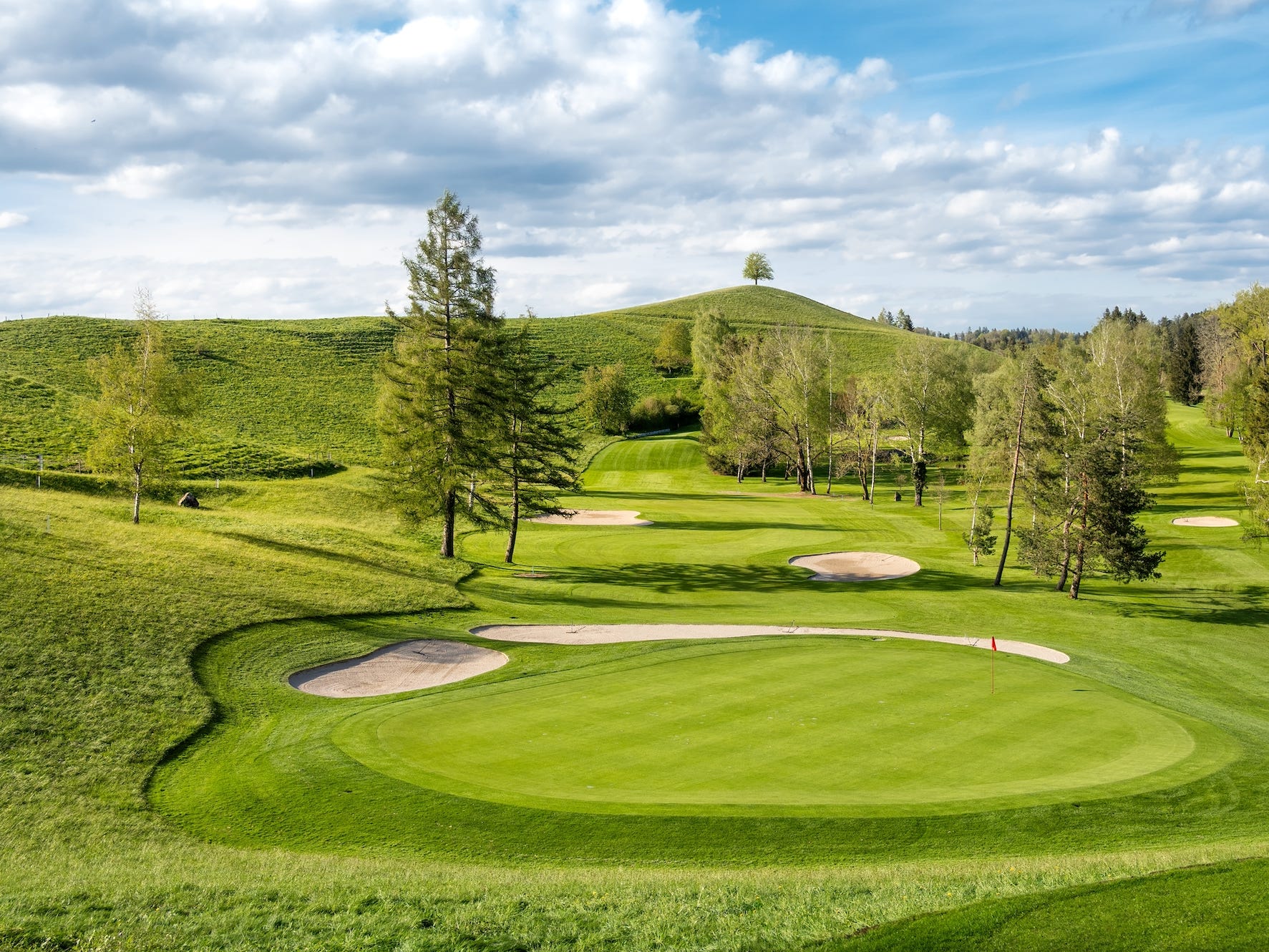 A pristine golf course on a cloudy day with blue skies.