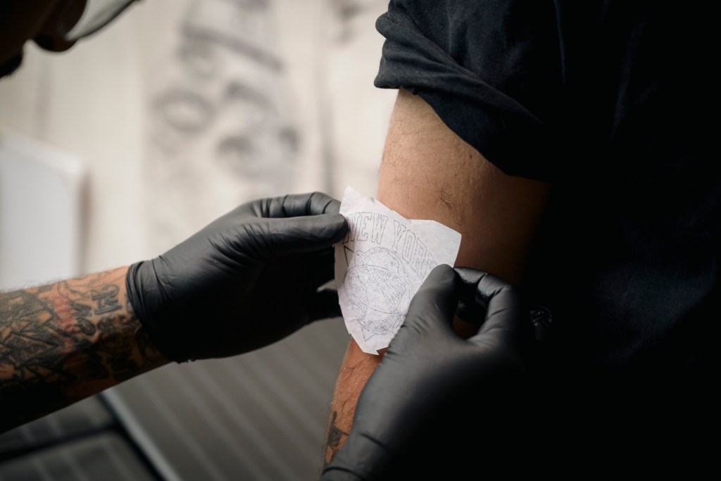 Nikhil Dhanani, a Queens resident, is getting a tattoo with the Knicks basketball logo by Steven Avalos, .
a Brooklyn tattoo artist, in his studio.