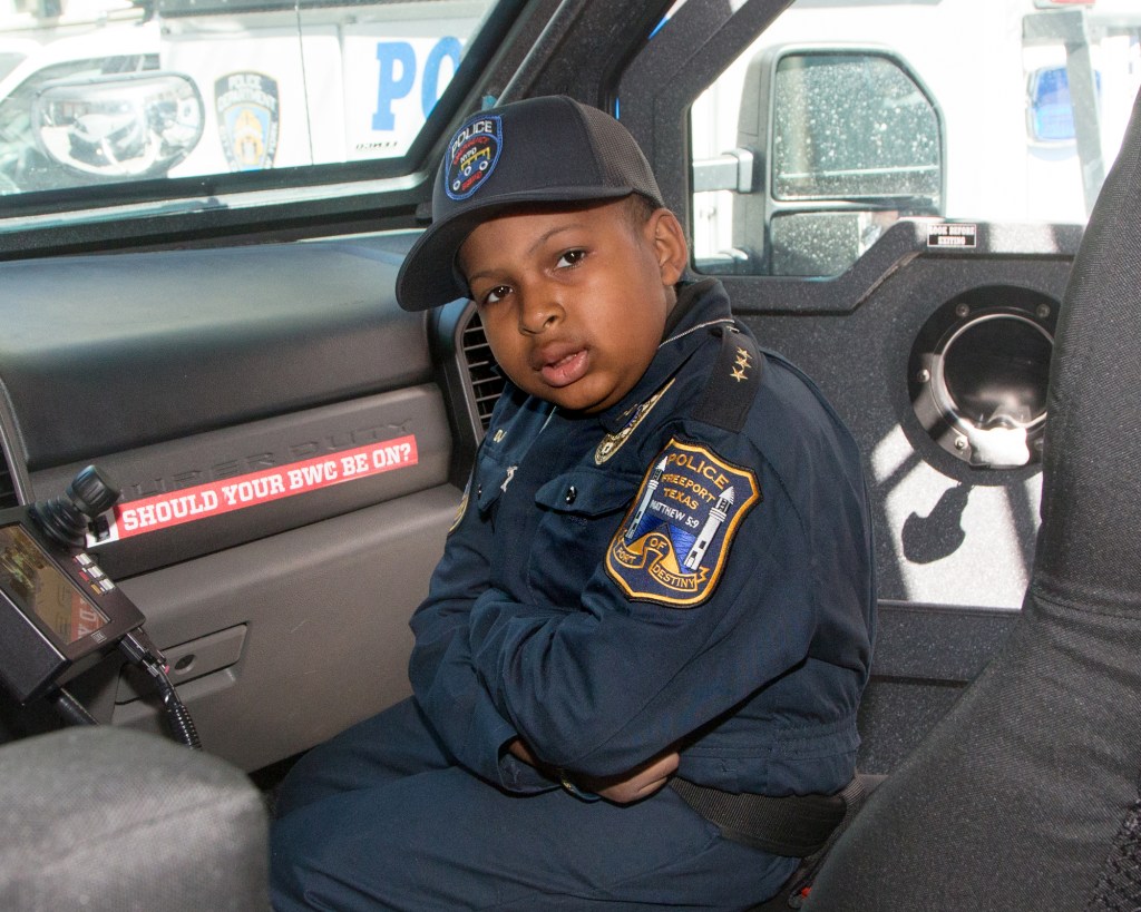 A 10-year-old Daniel wears a police uniform in a squad car.