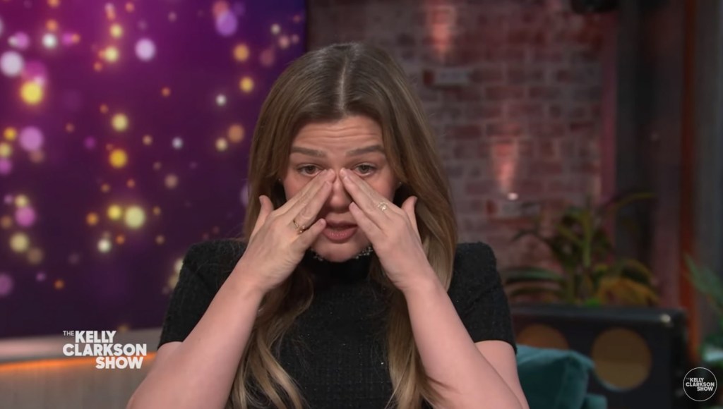 Kelly Clarkson wipes away tears, she's wearing black top.