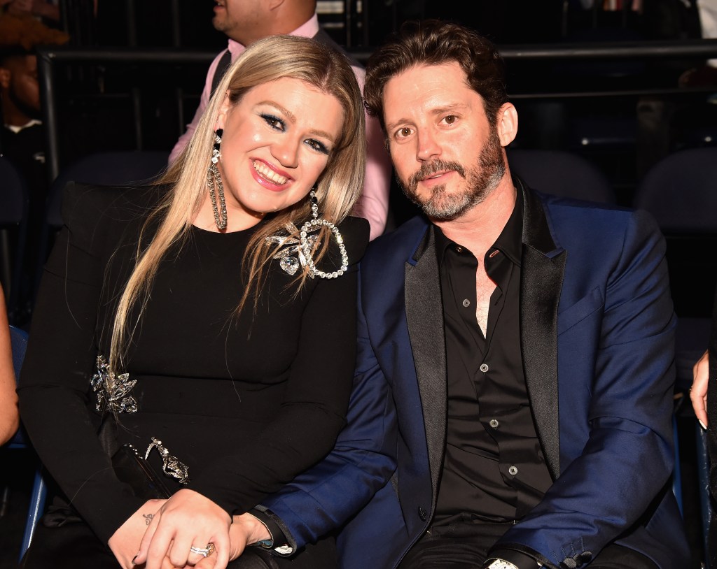 Kelly Clarkson in a black dress with embellishment, Brandon Blackstock in a navy blue suit with a black shirt.