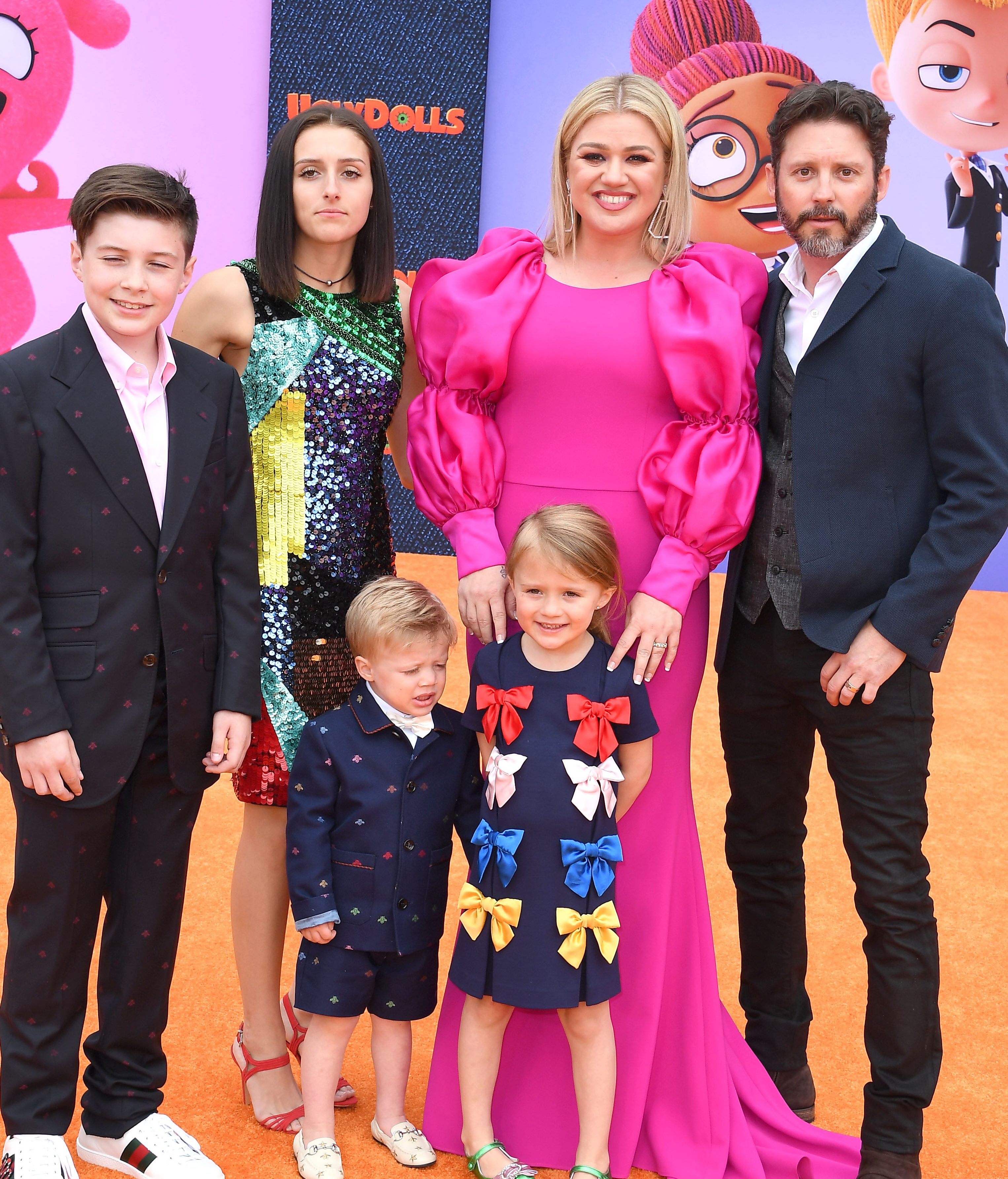 Seth Blackstock in a black suit and pink shirt, Savannah Blackstock in a multi-color sequined minidress, Remy Blackstock in a navy blue short suit, River Rose Blackstock in a navy blue dress with multi-color bows, Kelly Clarkson in a full-length hot pink dress with puffed sleeves, Brandon Blackstock in a black suit and white shirt.