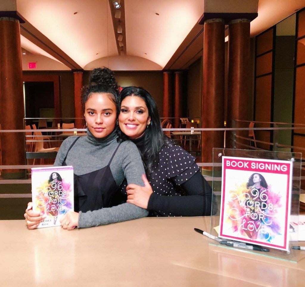 Ava Dash and Rachel Roy sit and embrace at a book signing. 