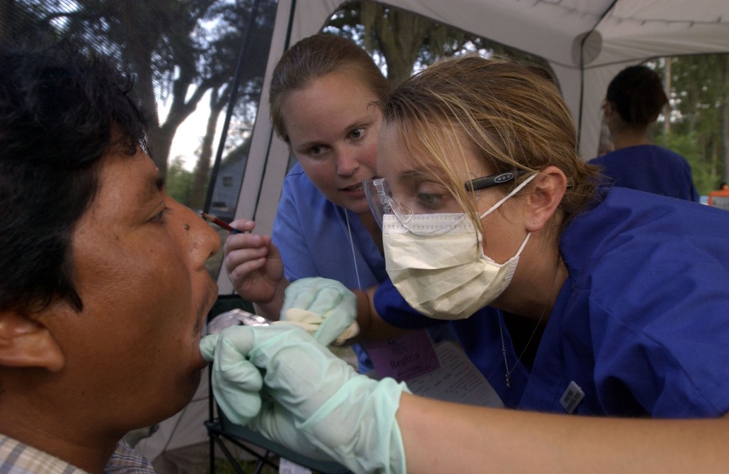 Darton College dental hygiene students Regina Schirato and Brooke Wenck give a farm worker a dental exam Wednesday evening, June 18, 2003, in a migrant farmer camp near Moultrie, Georgia. 