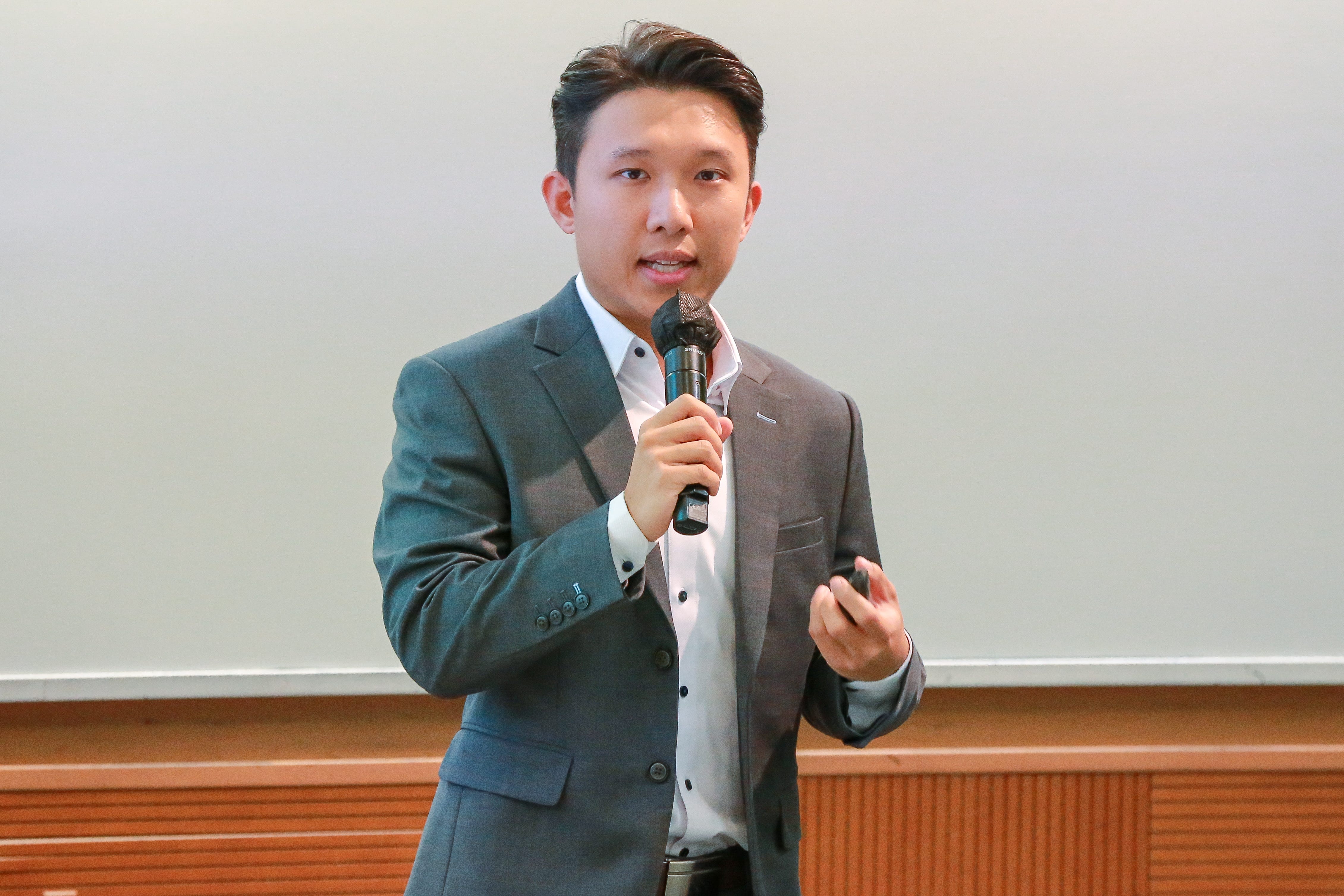 A young man wearing a suit speaking into a microphone.