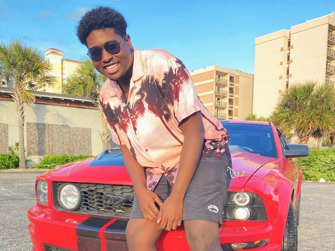 Corvon Burgess poses in sunglasses in front of a red car.
