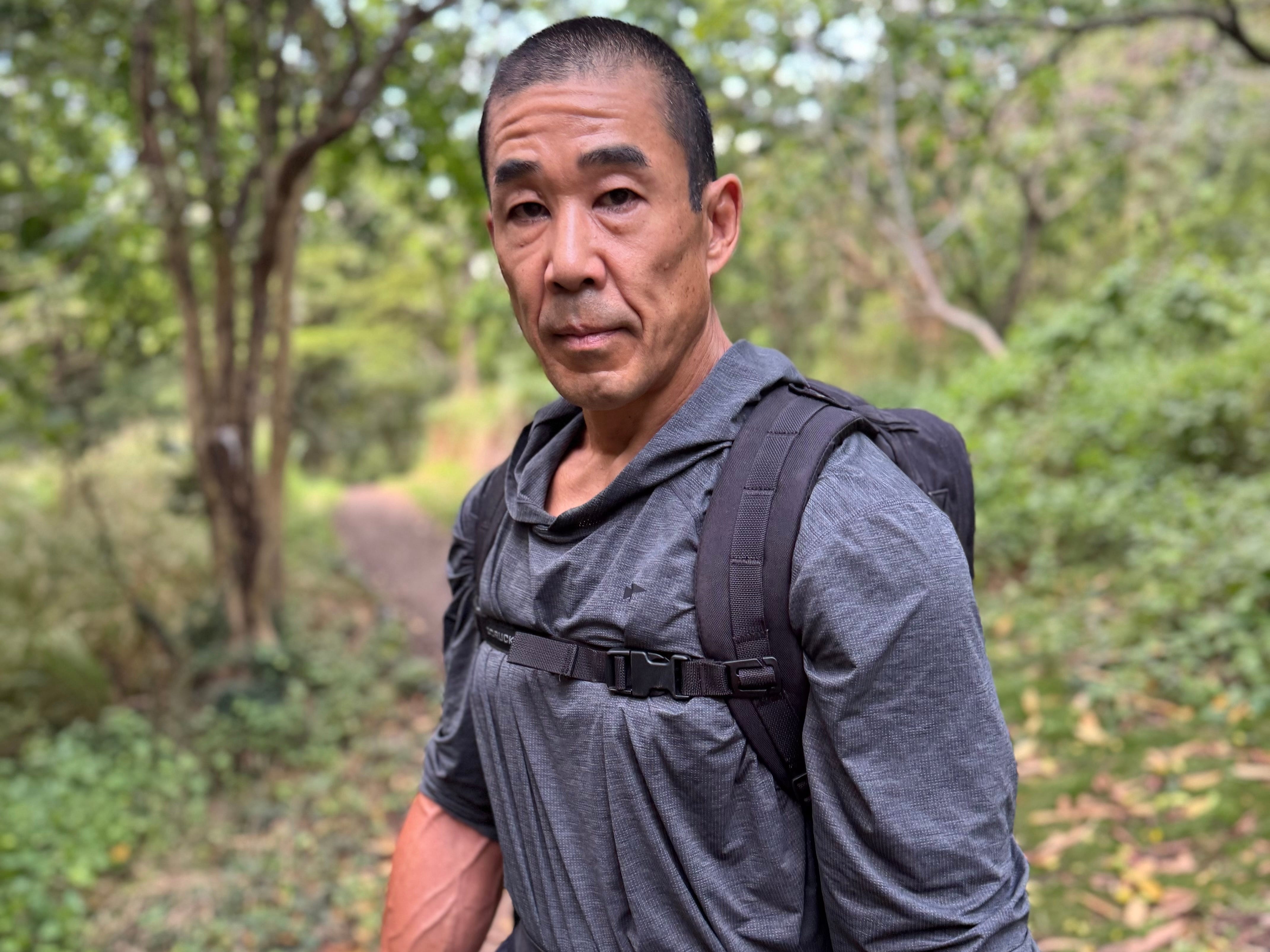 An athletic older man carries a weighted backpack on an outdoor trail.