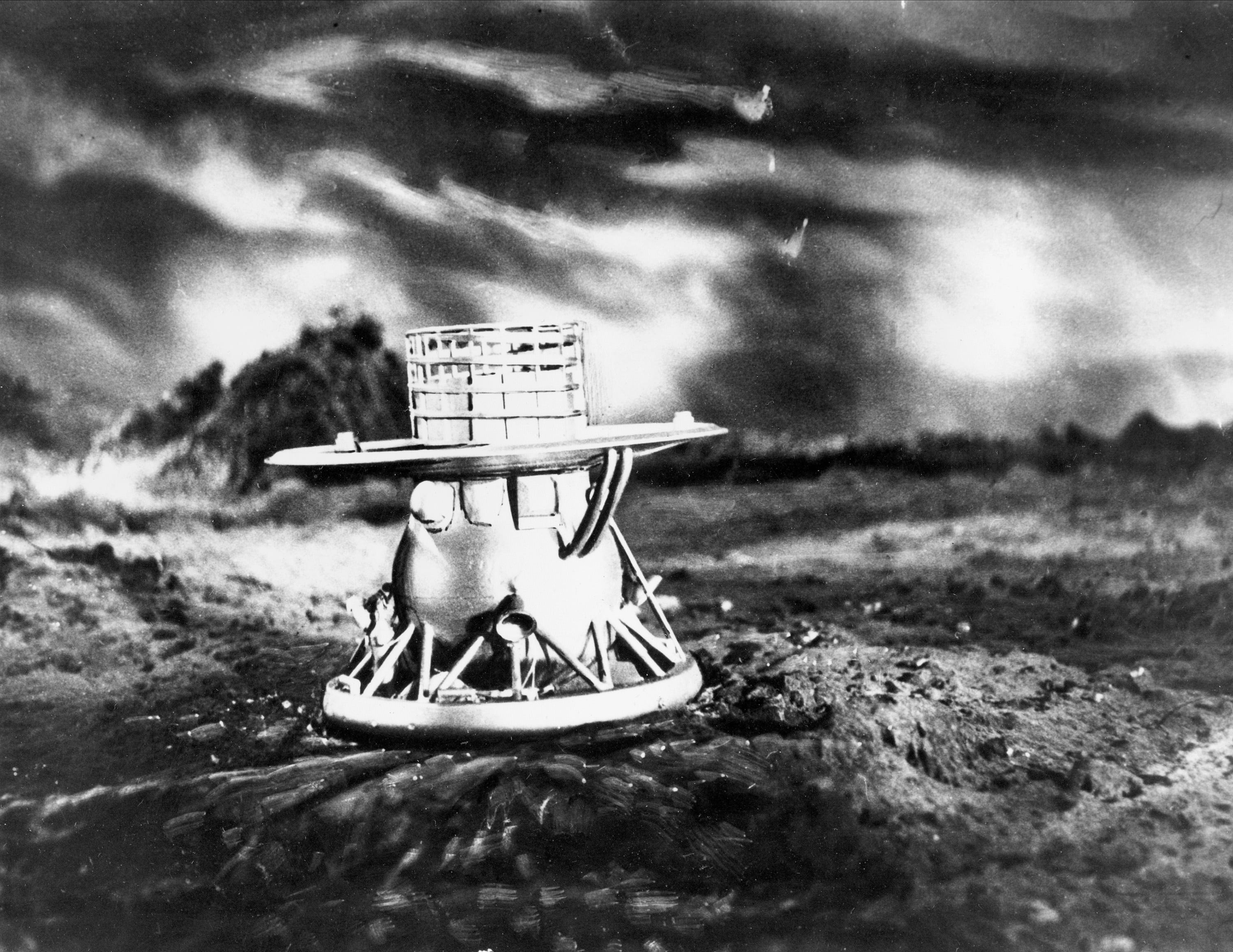 spacecraft replica shaped like a ball mounted on flat circular platform with a cylinder on top of it sitting on a diorama surface of venus