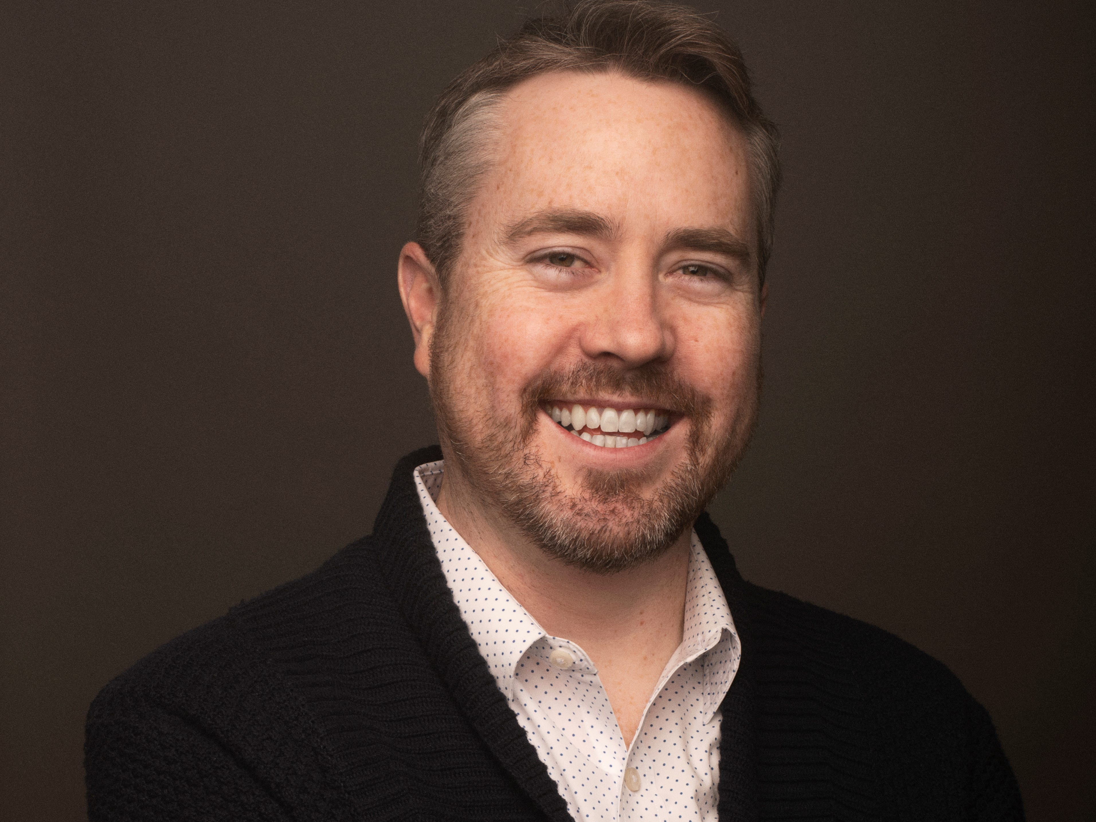 Ben Grubbs headshot wearing a black sweater and white polka-dotted shirt.