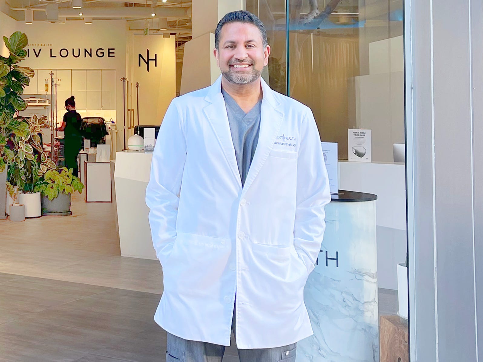 Darshan Shah in a white lab coat, standing in front of his clinic, which reads "Next Health."