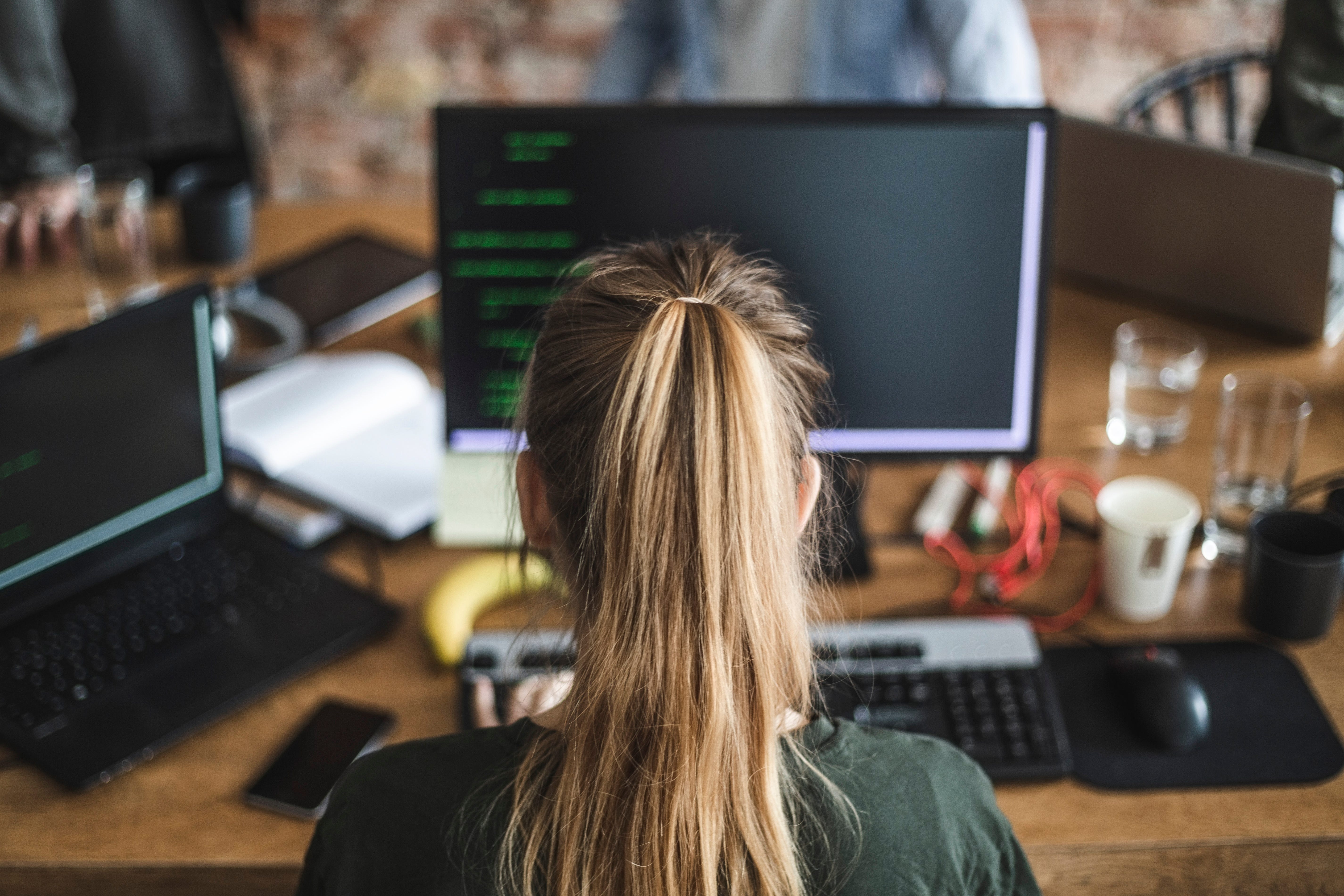 Blond female programmer coding over computer in startup company - stock photo