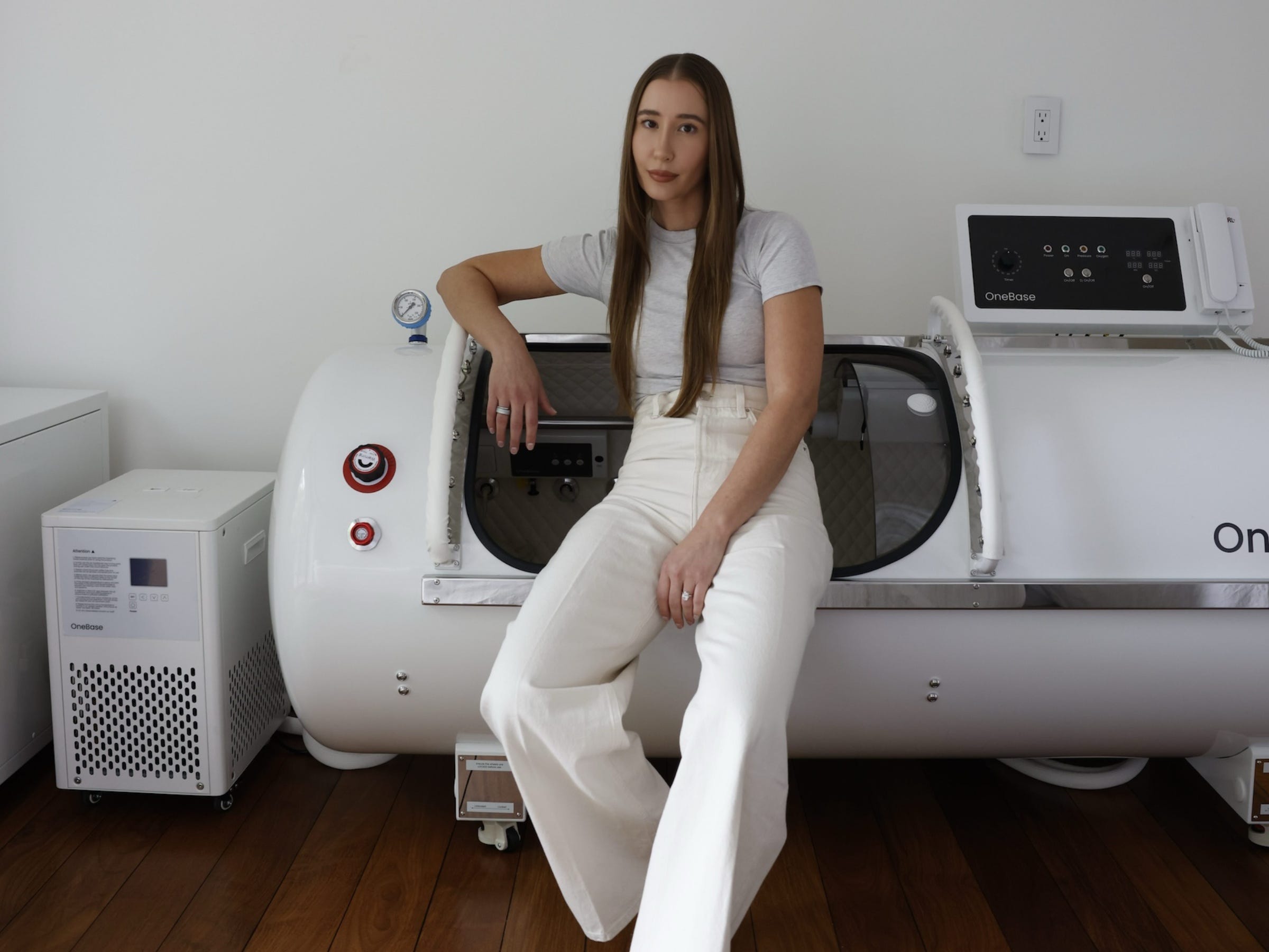 Kayla Barnes-Lentz dressed in all white, sat on her hyperbaric oxygen therapy machine.