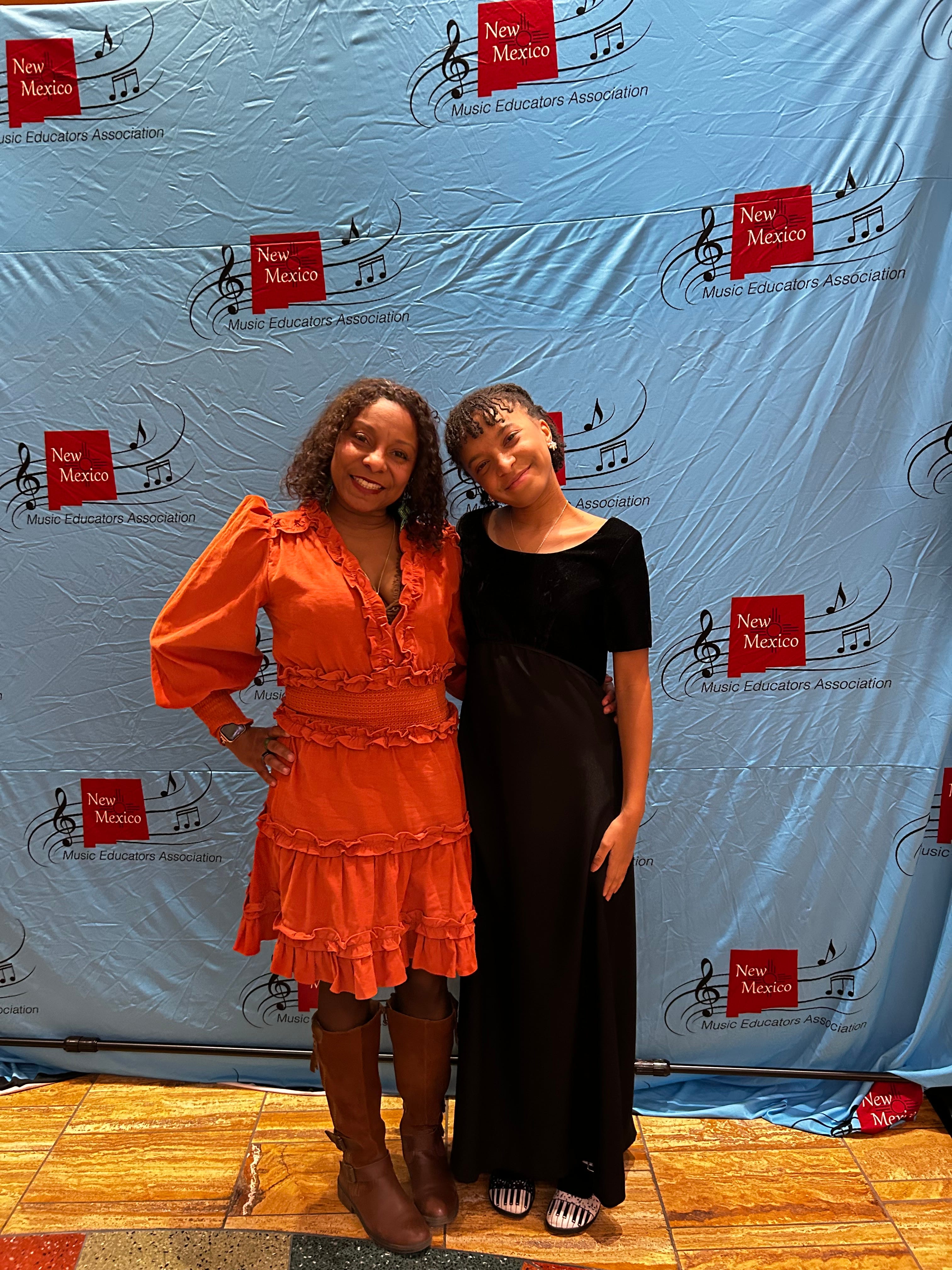 Ebonye Zeno wears an orange dress and poses with her daughter at a Music Educators Association event.