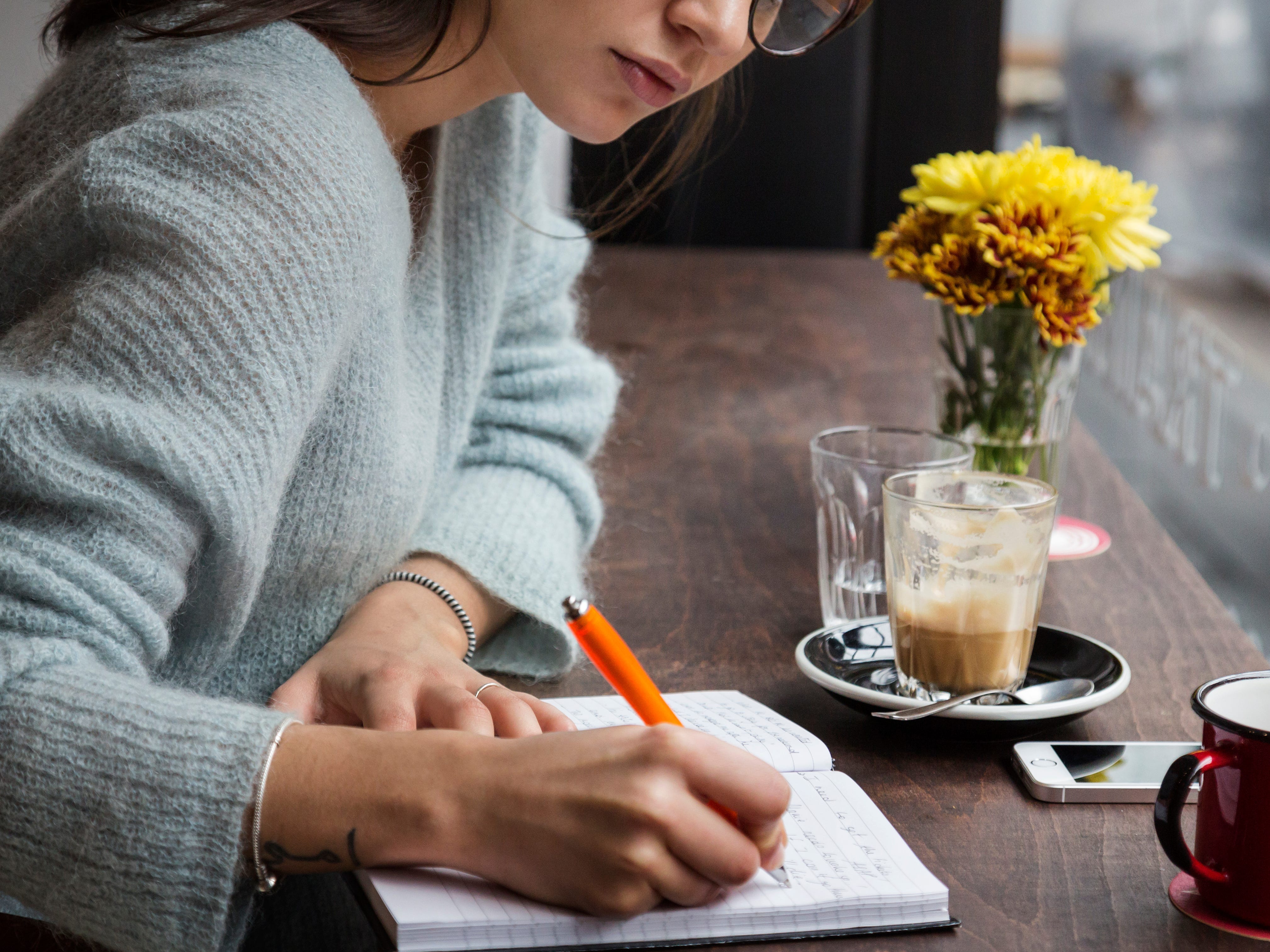 A person writing in a notebook at a coffee shop.