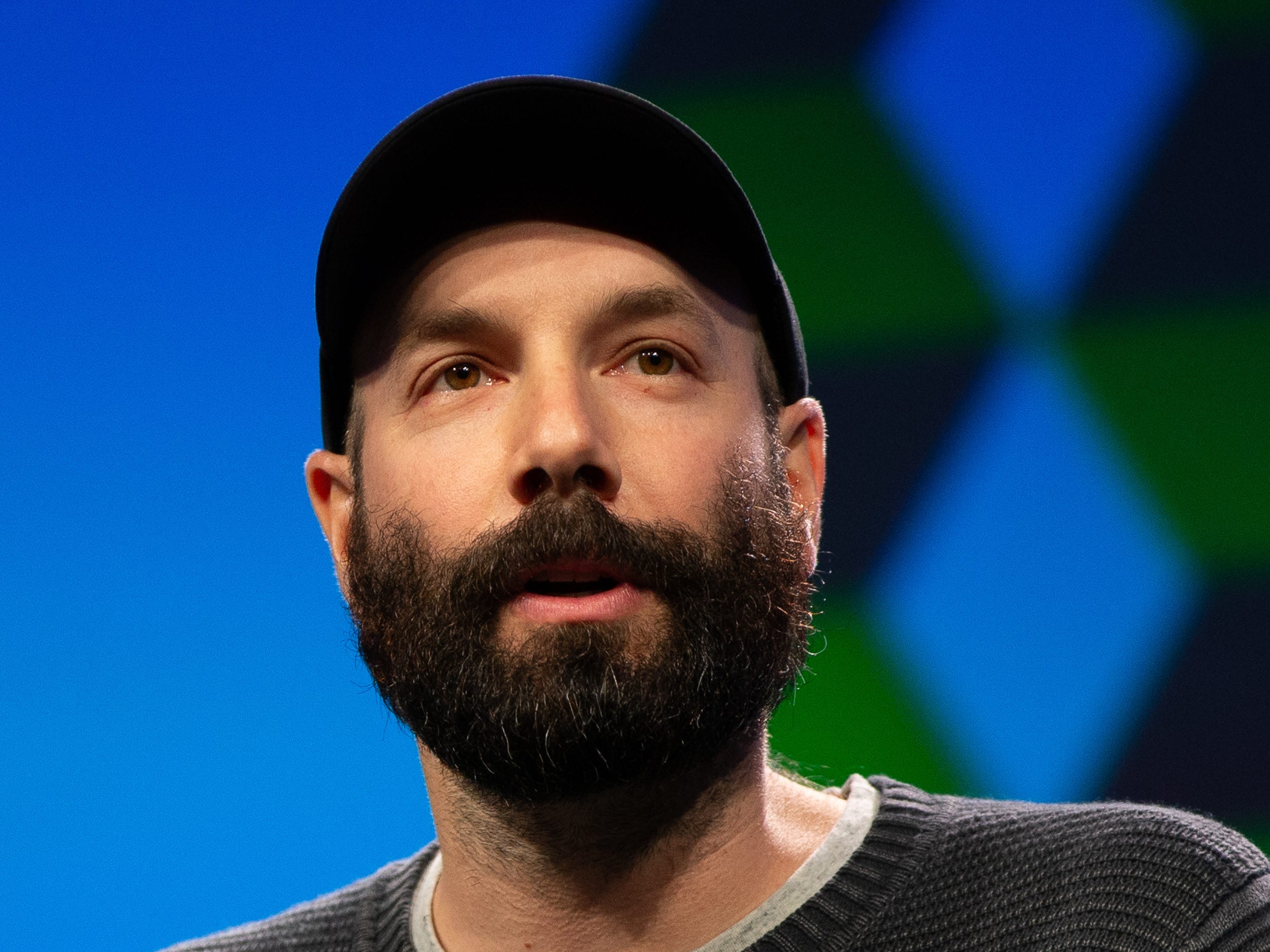 A closeup of Patreon CEO Jack Conte, wearing a baseball cap in front of a blue background.