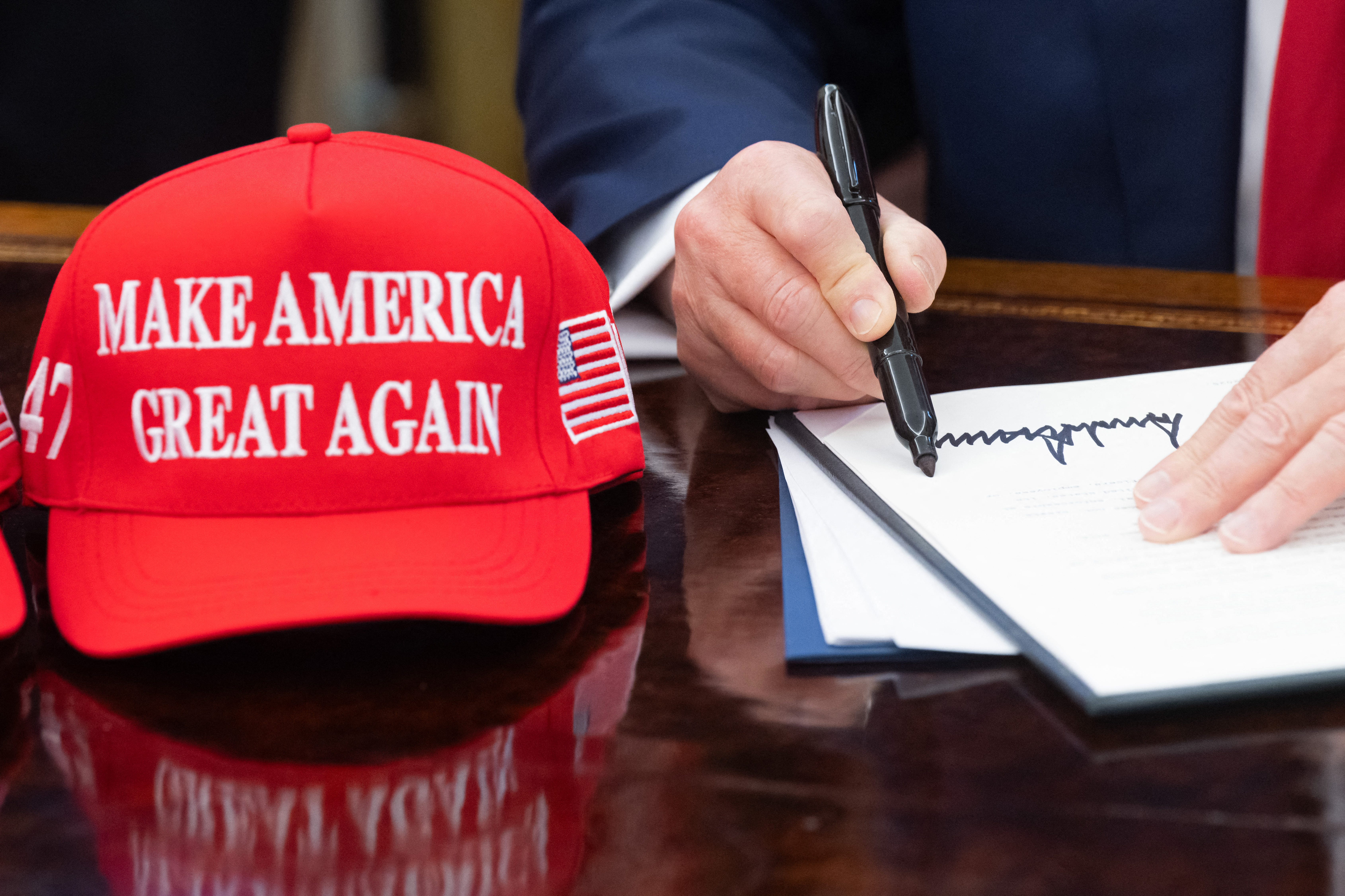 trump signs executive order next to maga hat