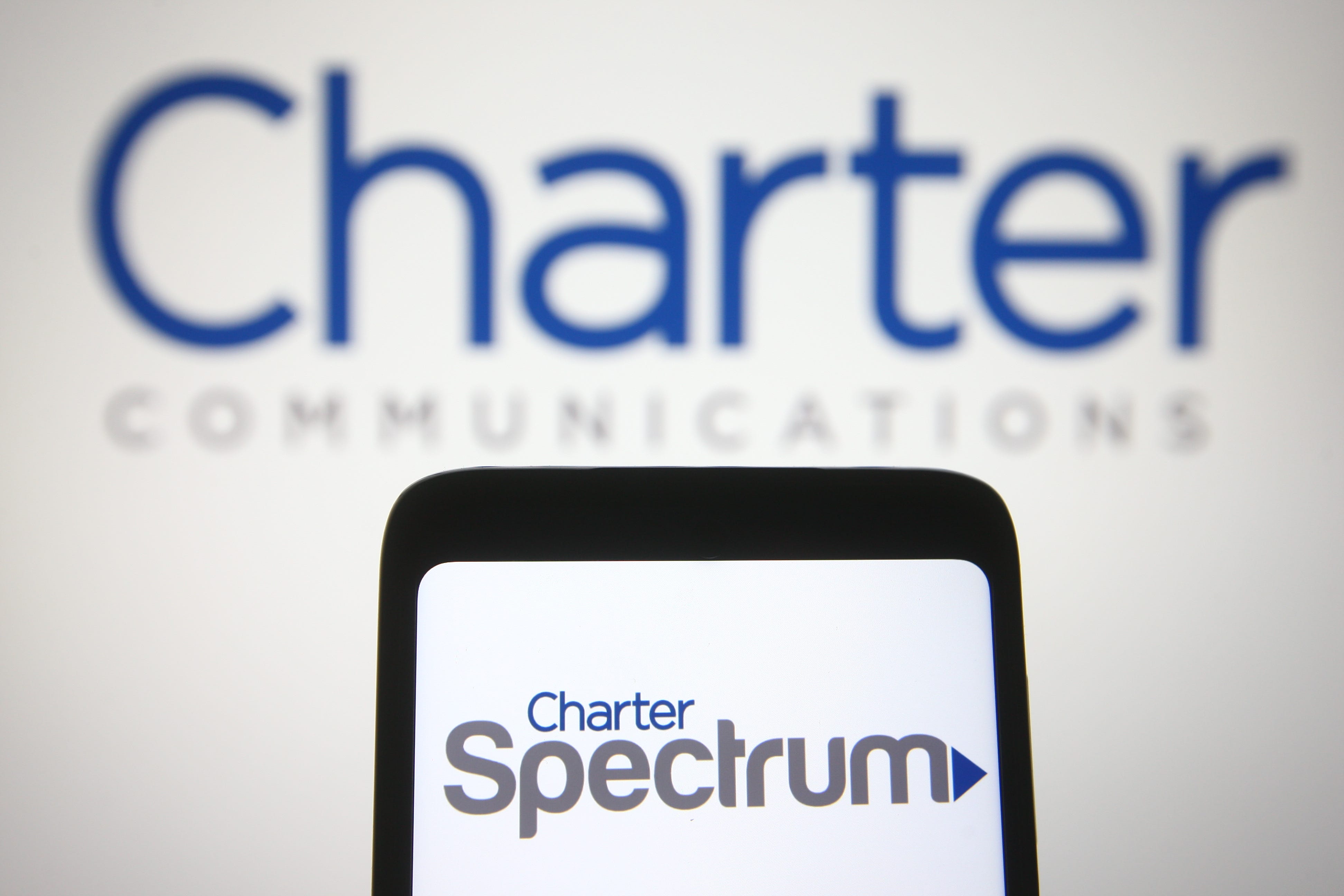 a phone screen with the Charter Spectrum logo is held up against a white background that says Charter Communications