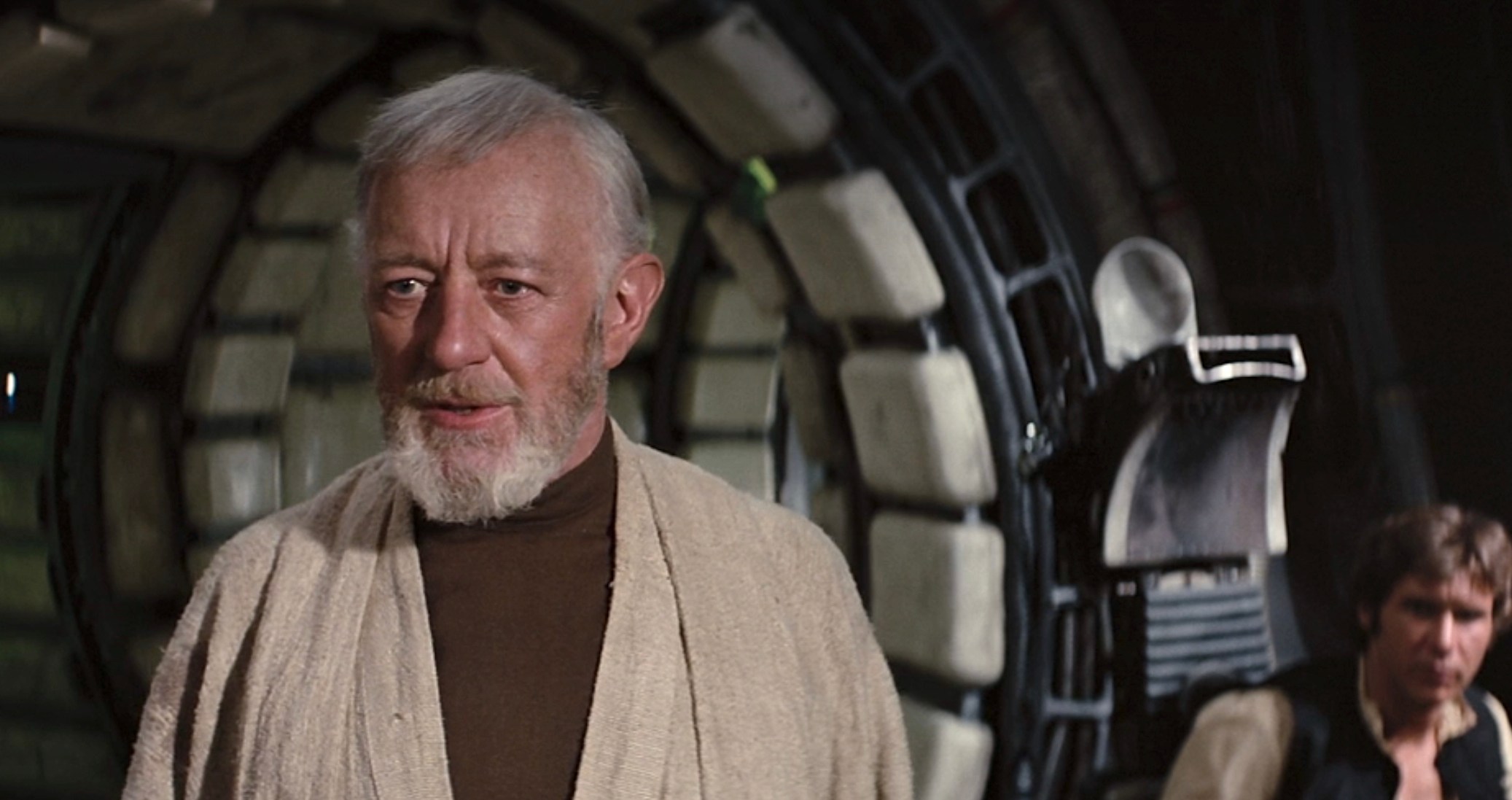 Alec Guinness as Obi-Wan Kenobi, standing in the Millennium Falcon with Han Solo (Harrison Ford) seated at a console in the background in Star Wars: Episode IV – A New Hope