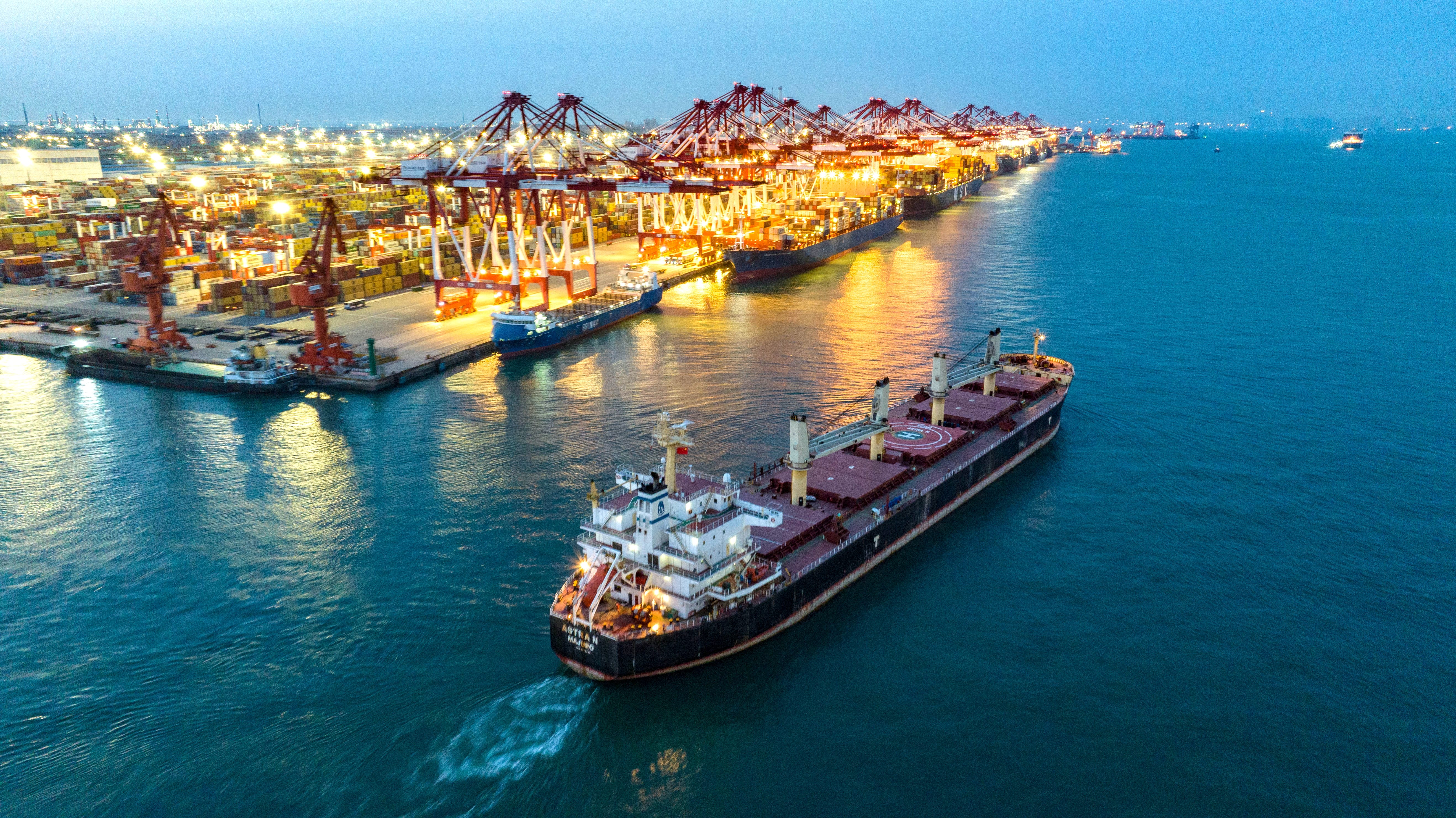 Container ship sails past a lit up port in China