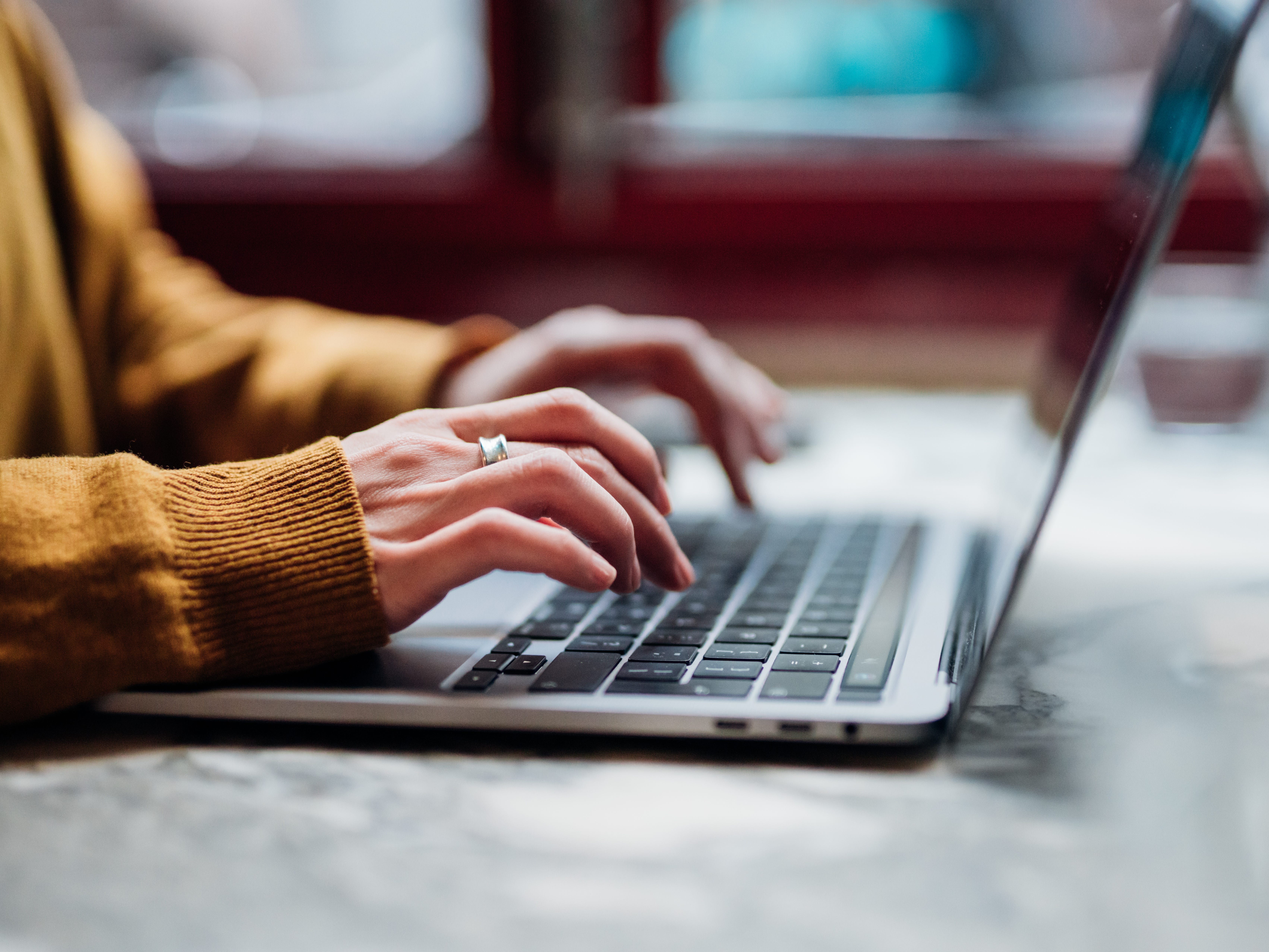 A woman in a beige sweater typing at a laptop.