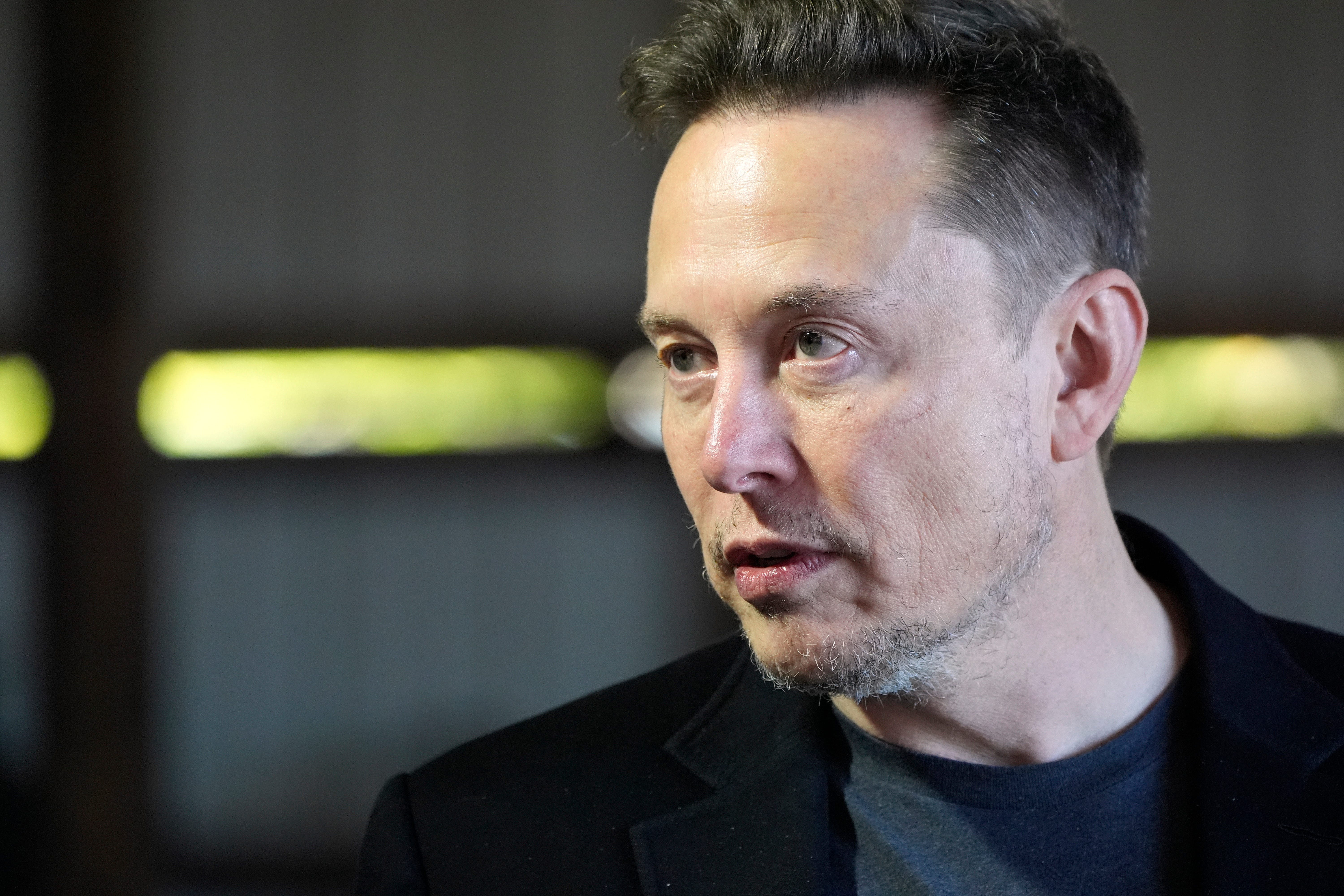 A close-up of Elon Musk in a black blazer and t-shirt.