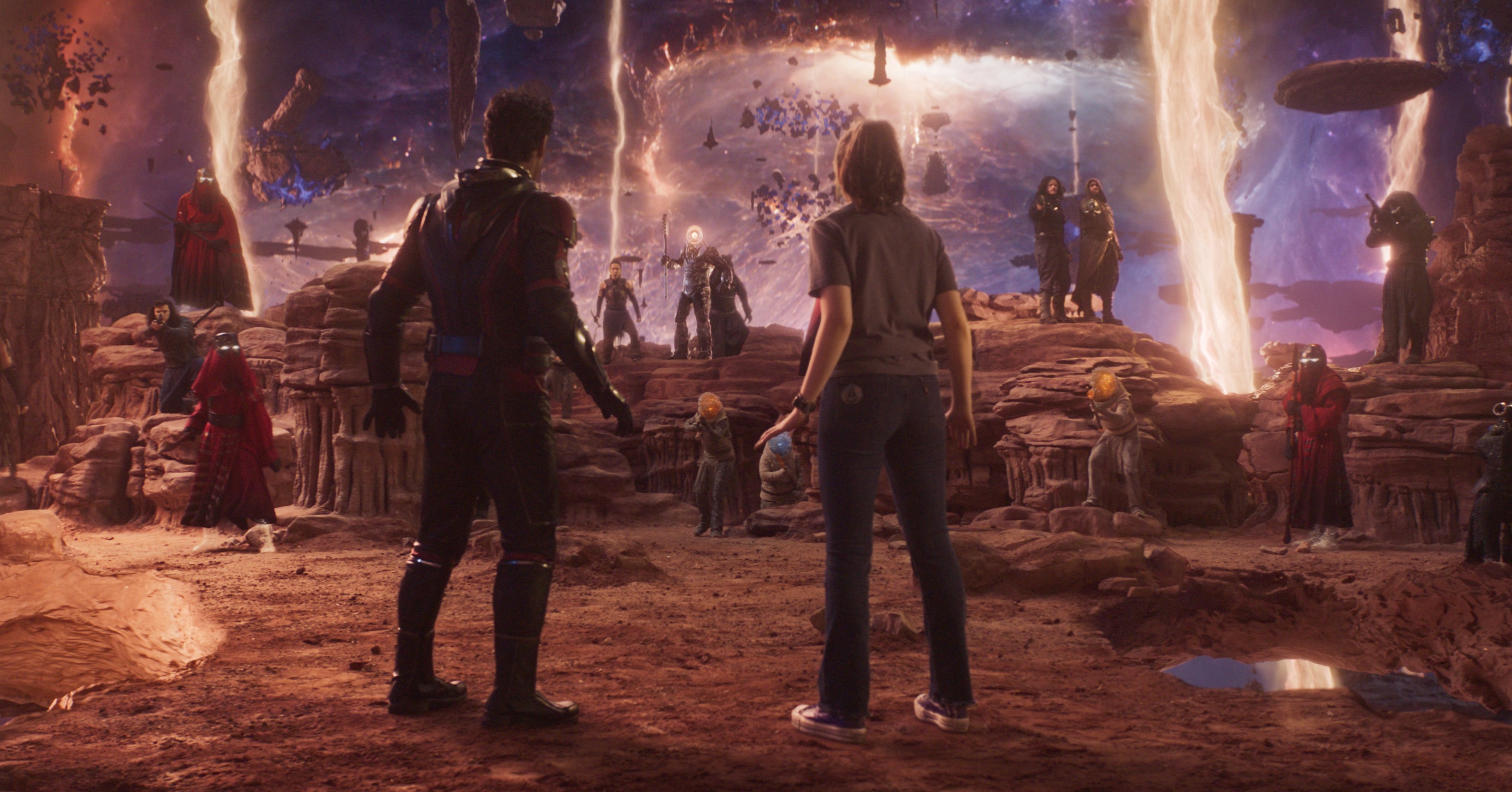 (L-R): Paul Rudd as Scott Lang/Ant-Man and Kathryn Newton as Cassandra “Cassie” Lang in Ant-Man and the Wasp: Quantumania. They stand stock still in an an alien landscape, surrounded by the place’s strange denizens.