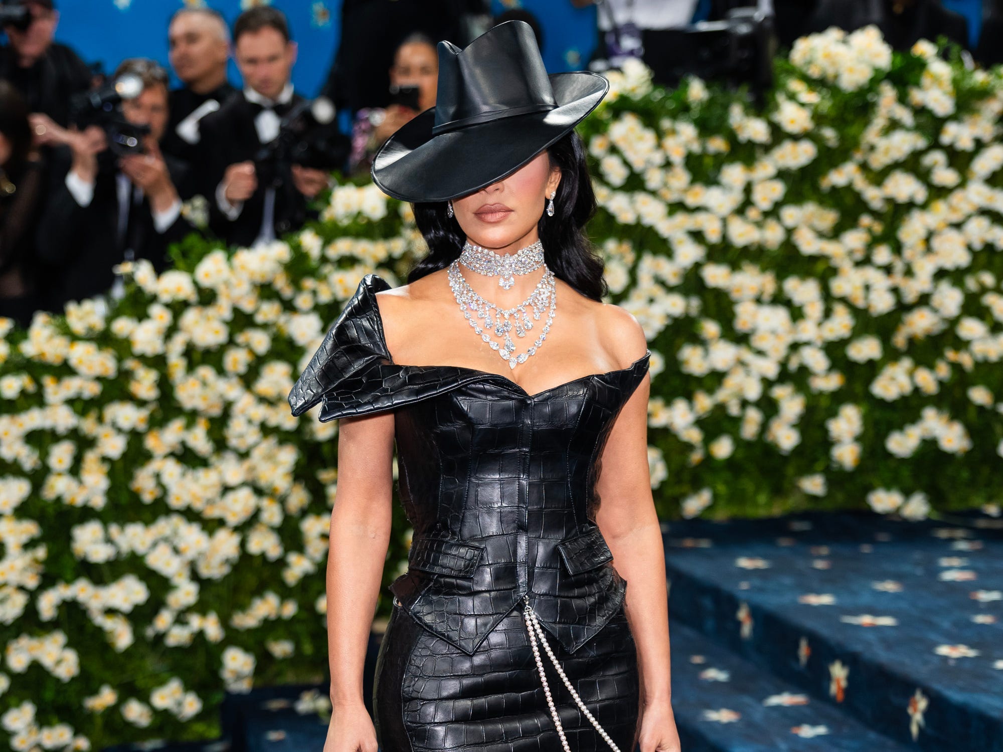 Kim Kardashian poses at the Met Gala in a leather dress and a hat that covers her eyes.