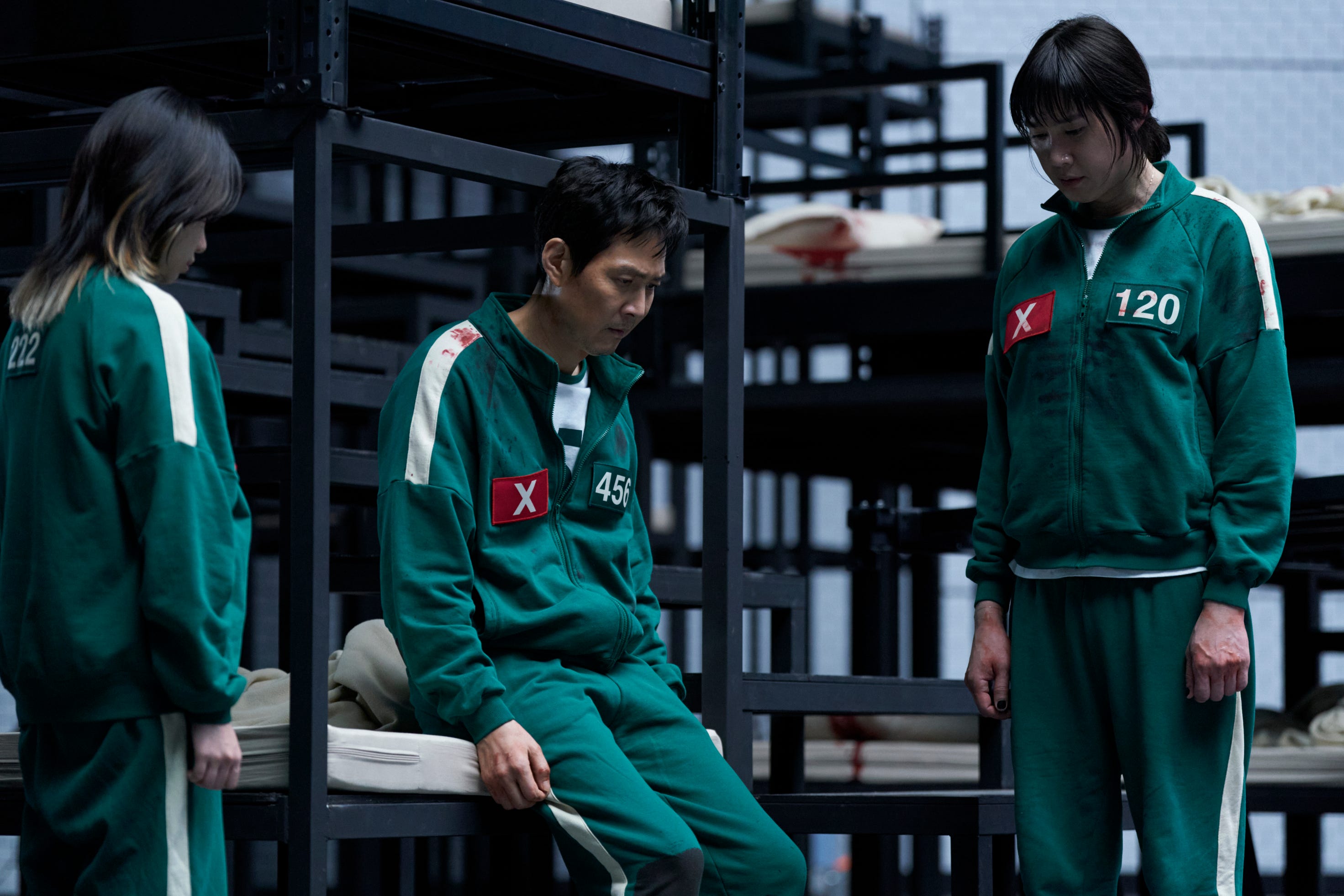 A still of "Squid Game" season three showing Park Sung-hoon as Cho Hyun-ju, Jo Yu-ri as Kim Jun-hee, and Lee Jung-jae as Seong Gi-hun in green jumpsuits.