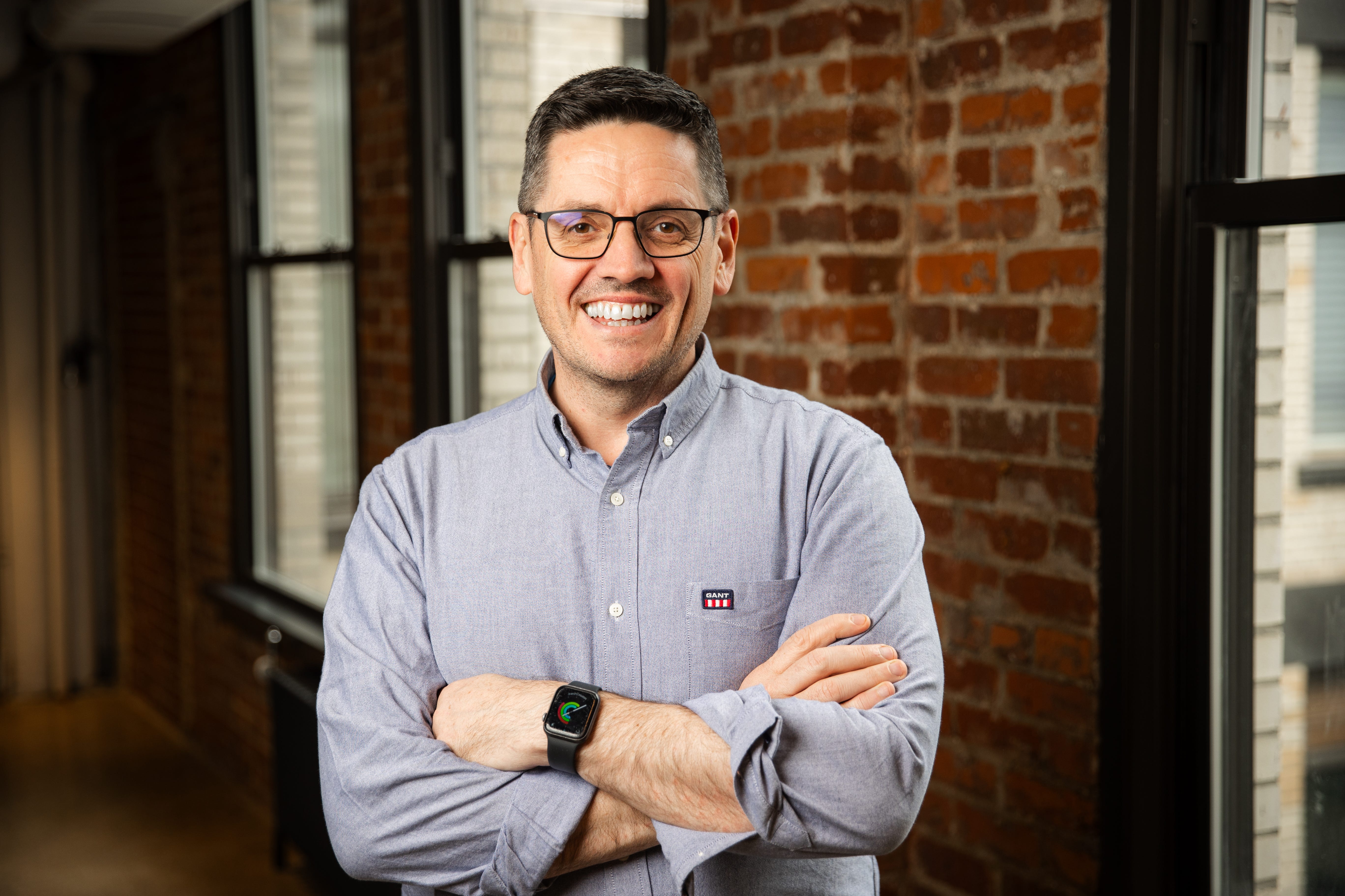 Fanatics' president of gaming, Conor Grant, smiles in an office against a brick background.