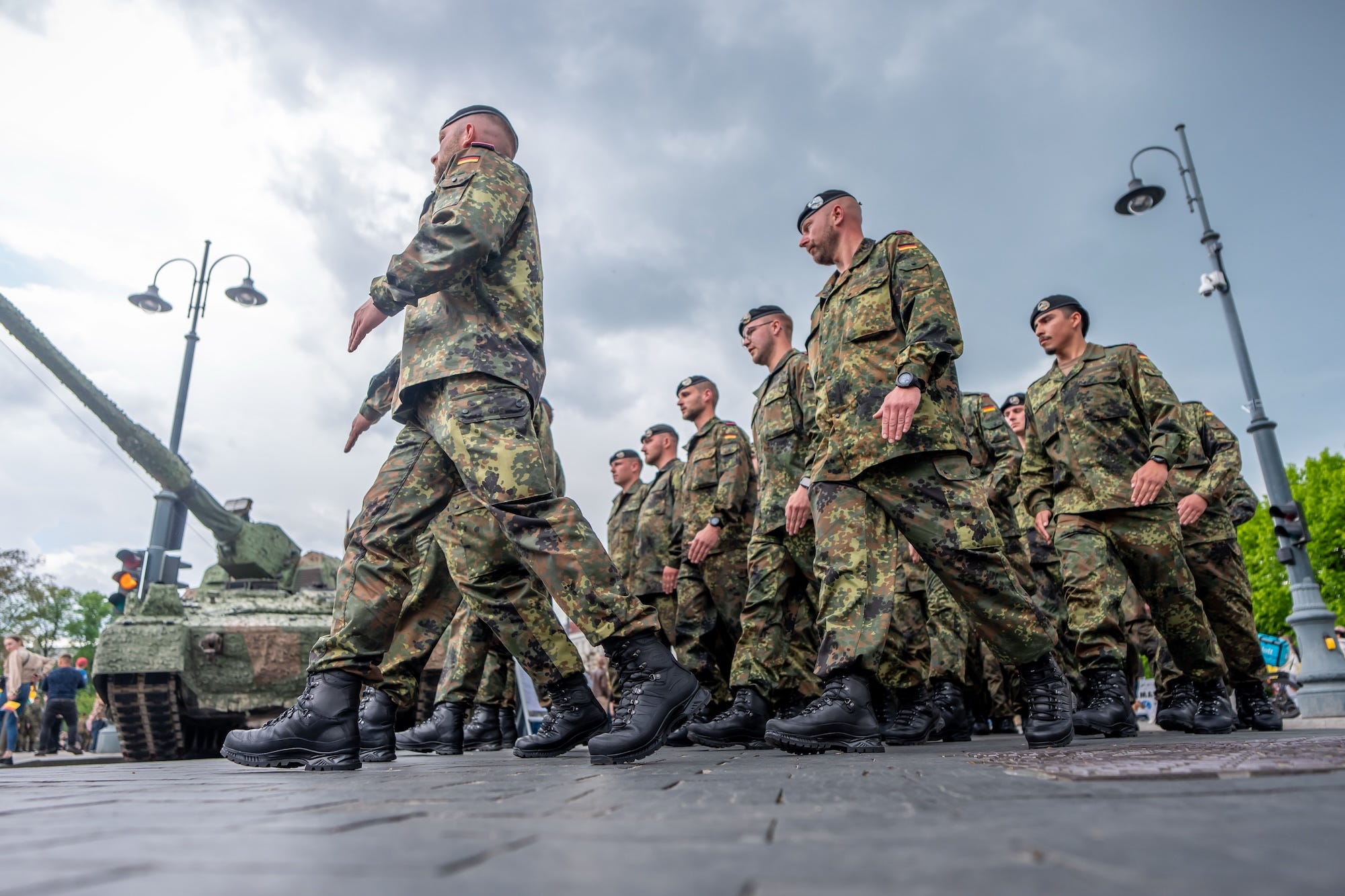 Men in black buits and combat gear with german flags on their upper arms walk under a grey sky