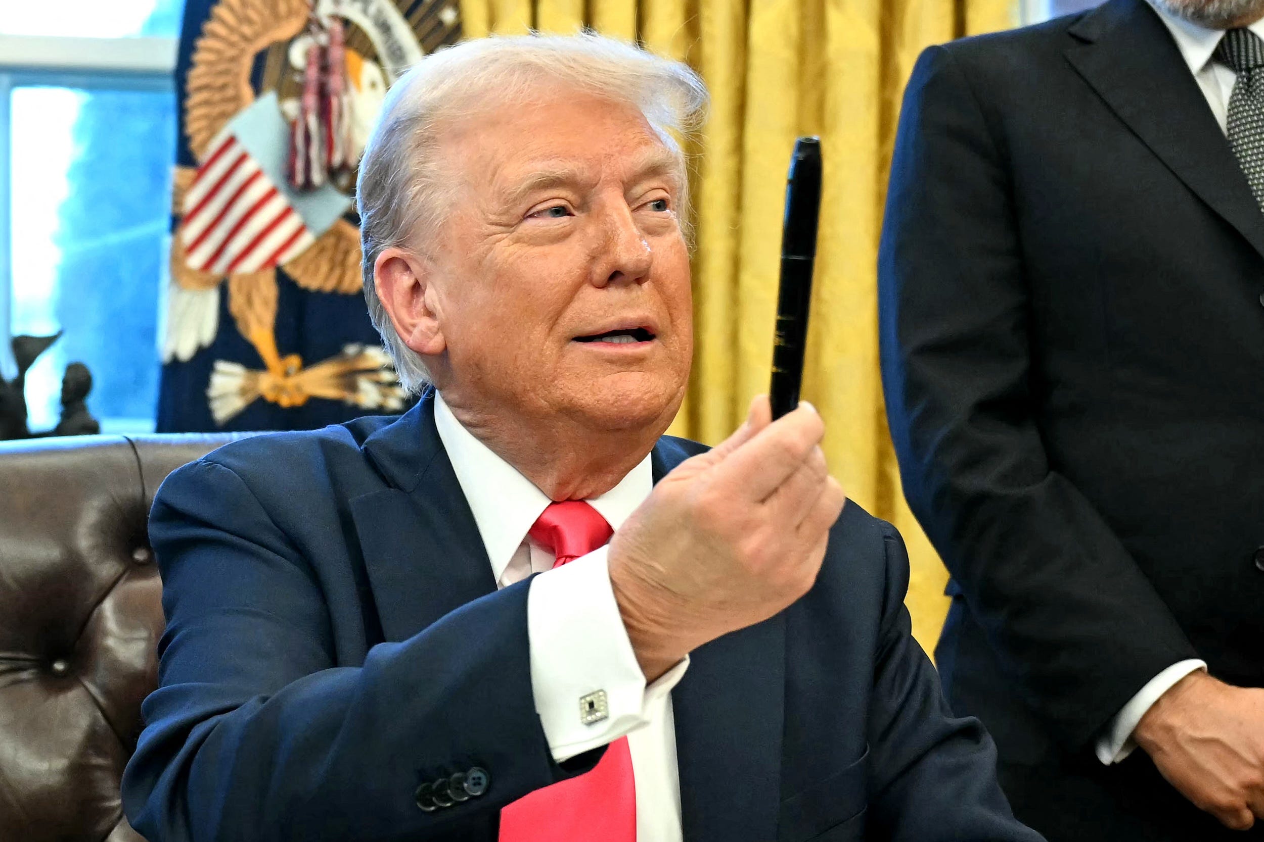 Donald Trump holds up a pen in the Oval Office