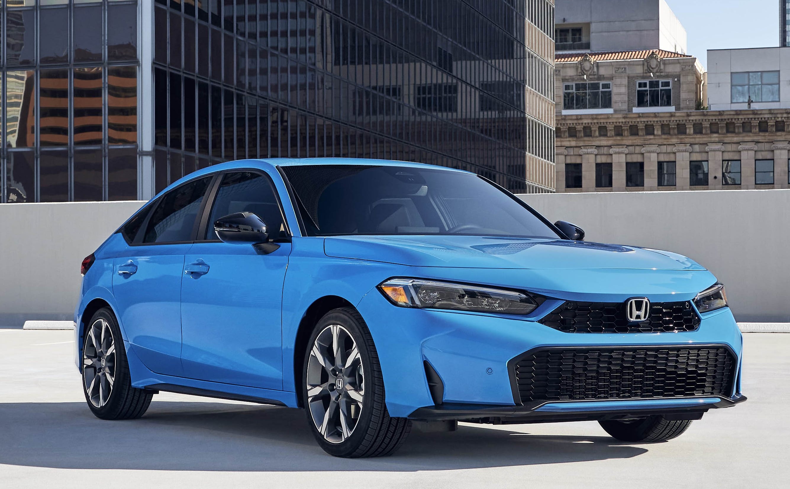 The right front corner of a blue 2025 Honda Civic Hatchback Sport Touring Hybrid parked in a parking deck.