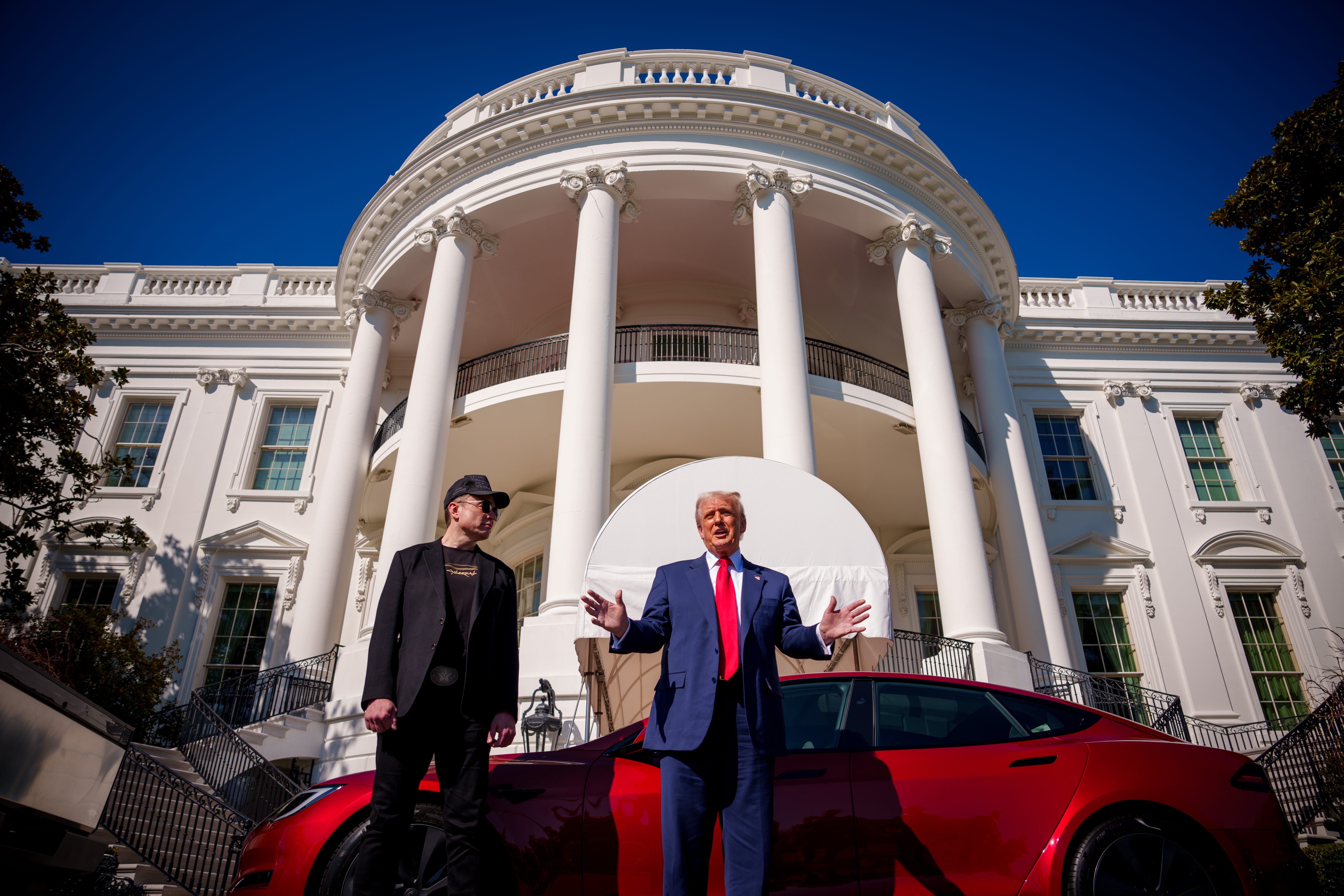 Donald Trump and Elon Musk stand on the White House lawn with a red Tesla
