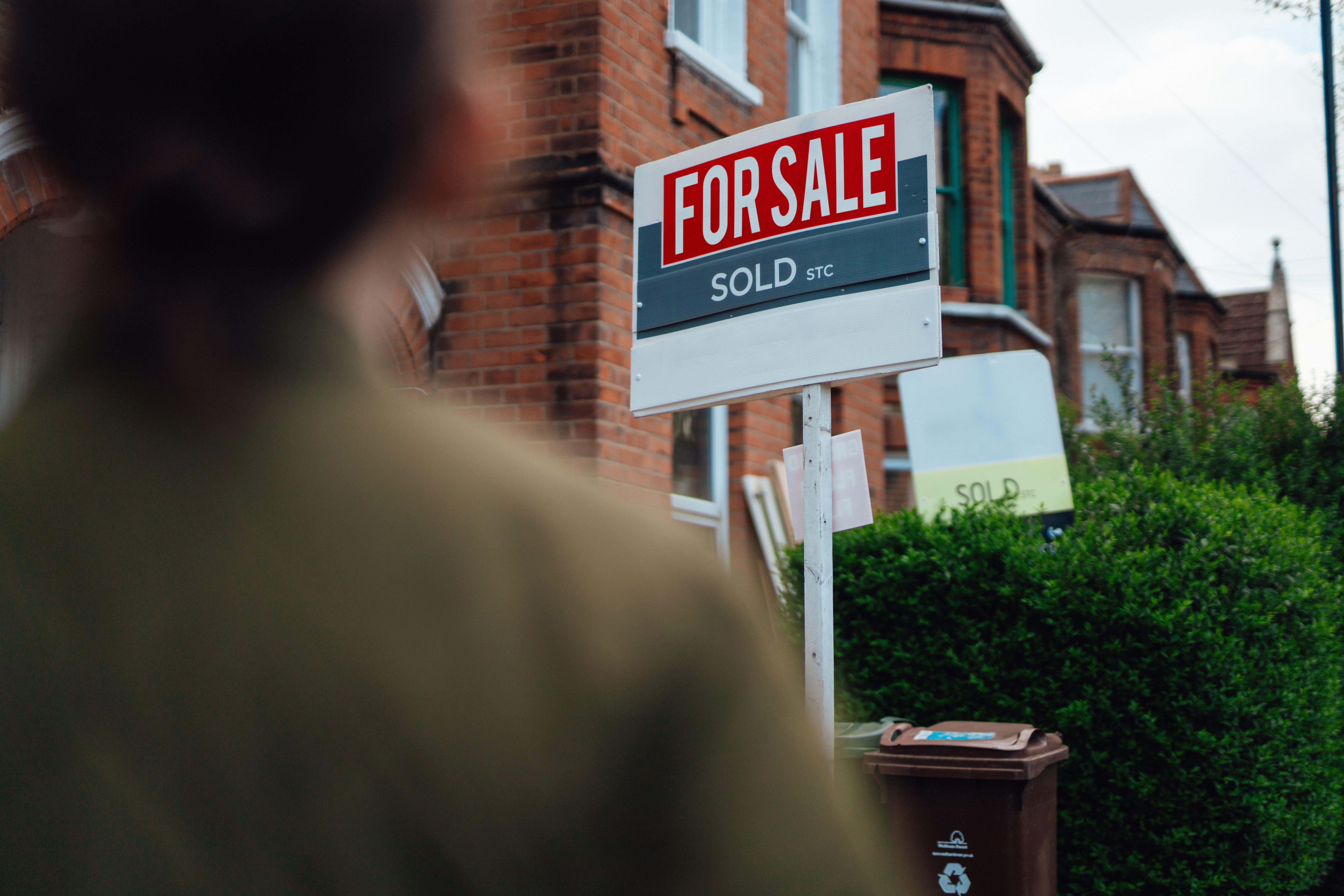 A woman standing in front of a for sale sign.