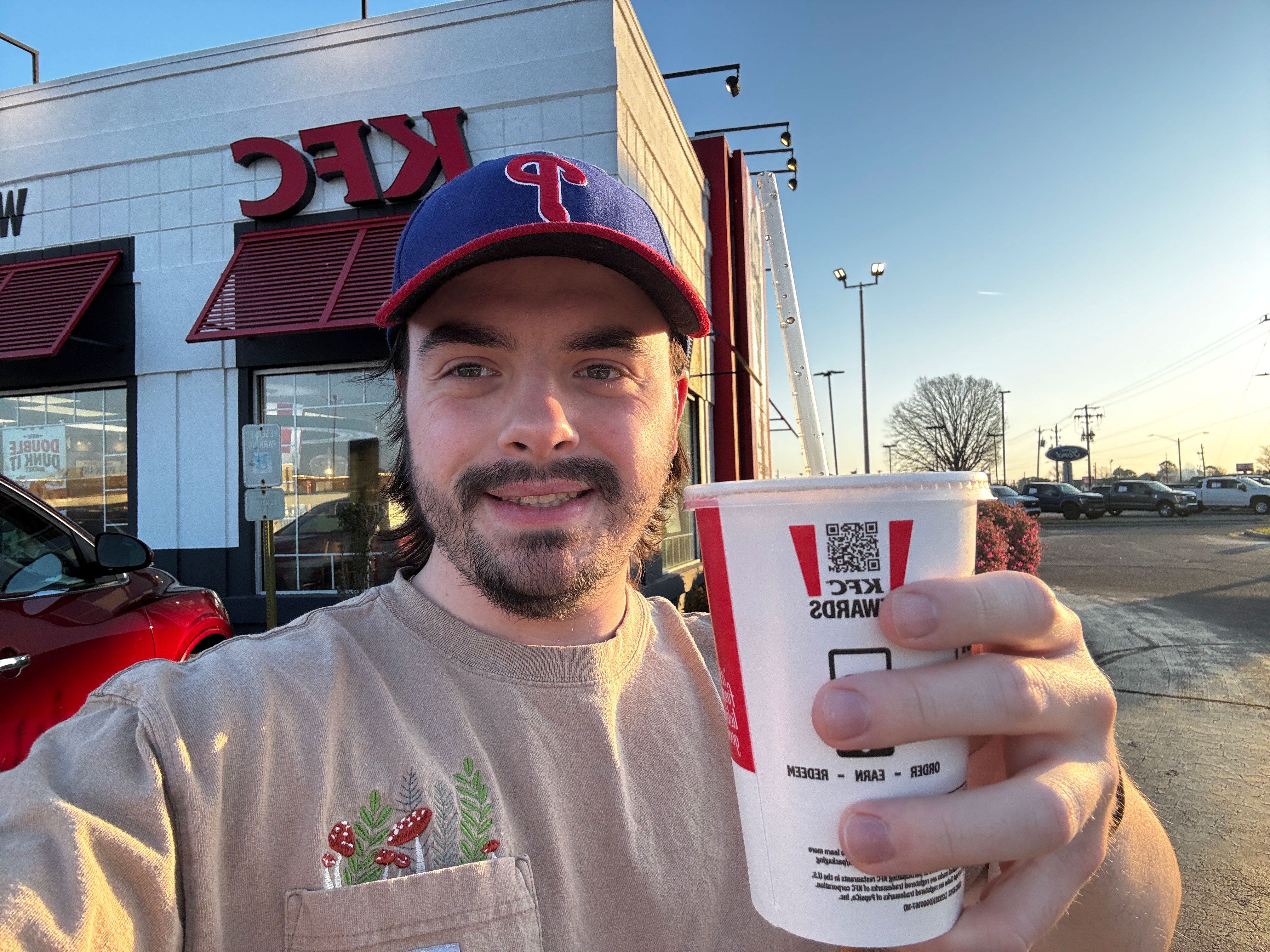 Dan holds a KFC cup and poses in front of a KFC restaurant.
