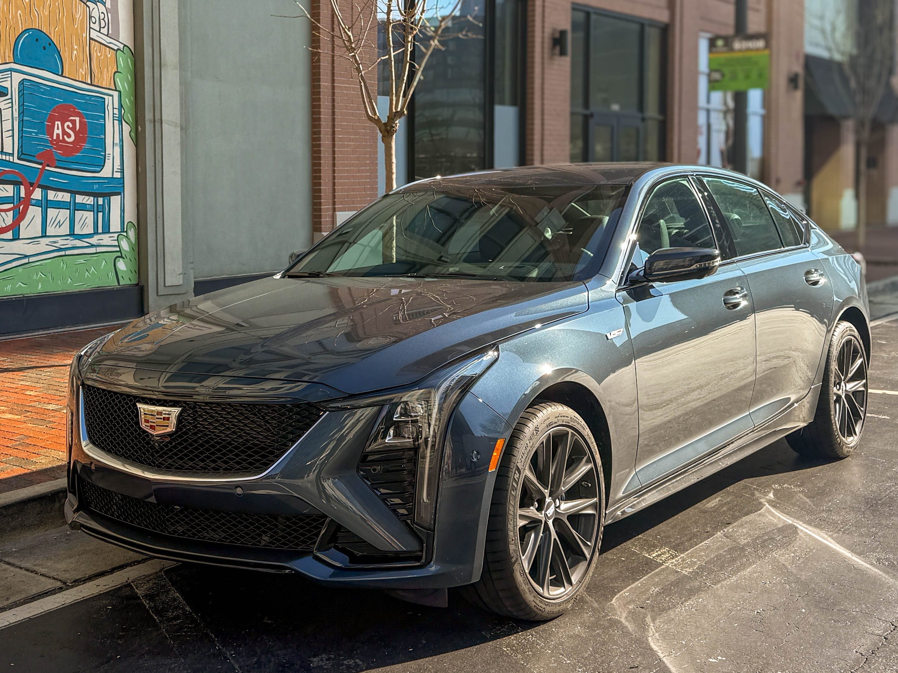 The left front corner of a gray 2025 Cadillac CT5-V sports sedan parked on the street.