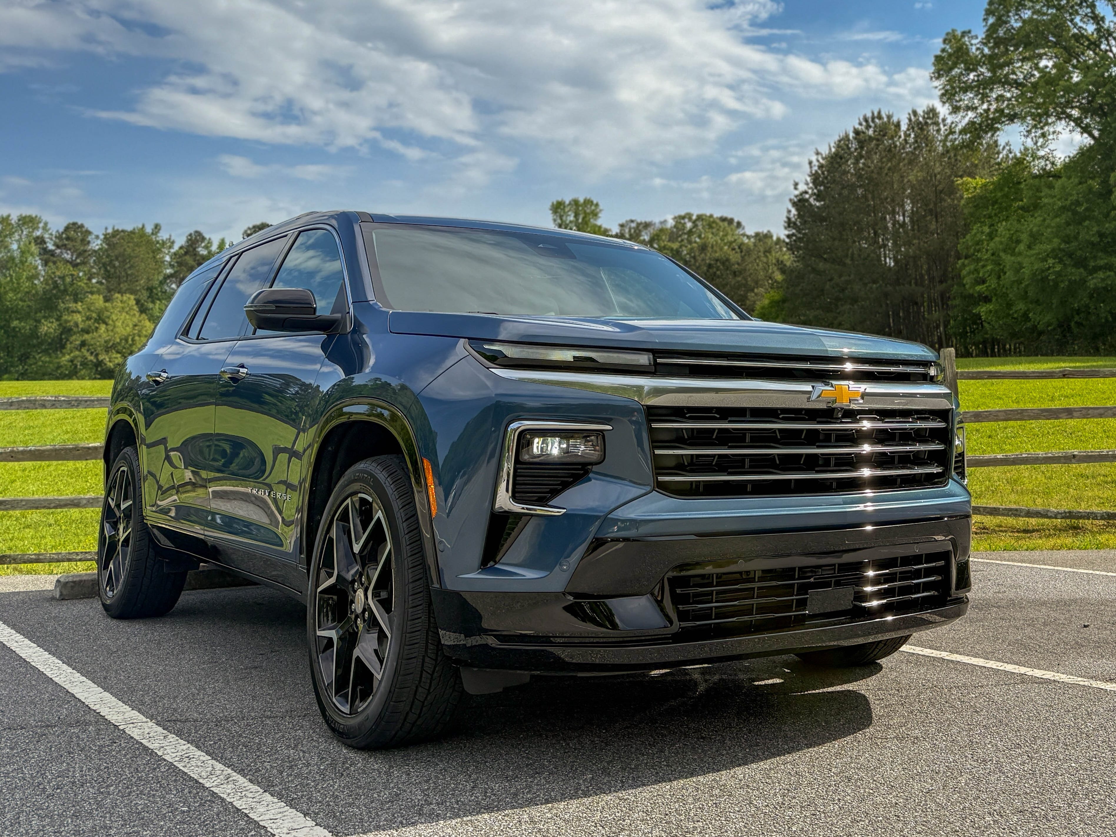 The right front of a blue 2025 Chevrolet Traverse High Country midsize family SUV parked by a field.