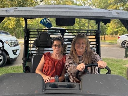 Two women pose while sitting in a utility vehicle.