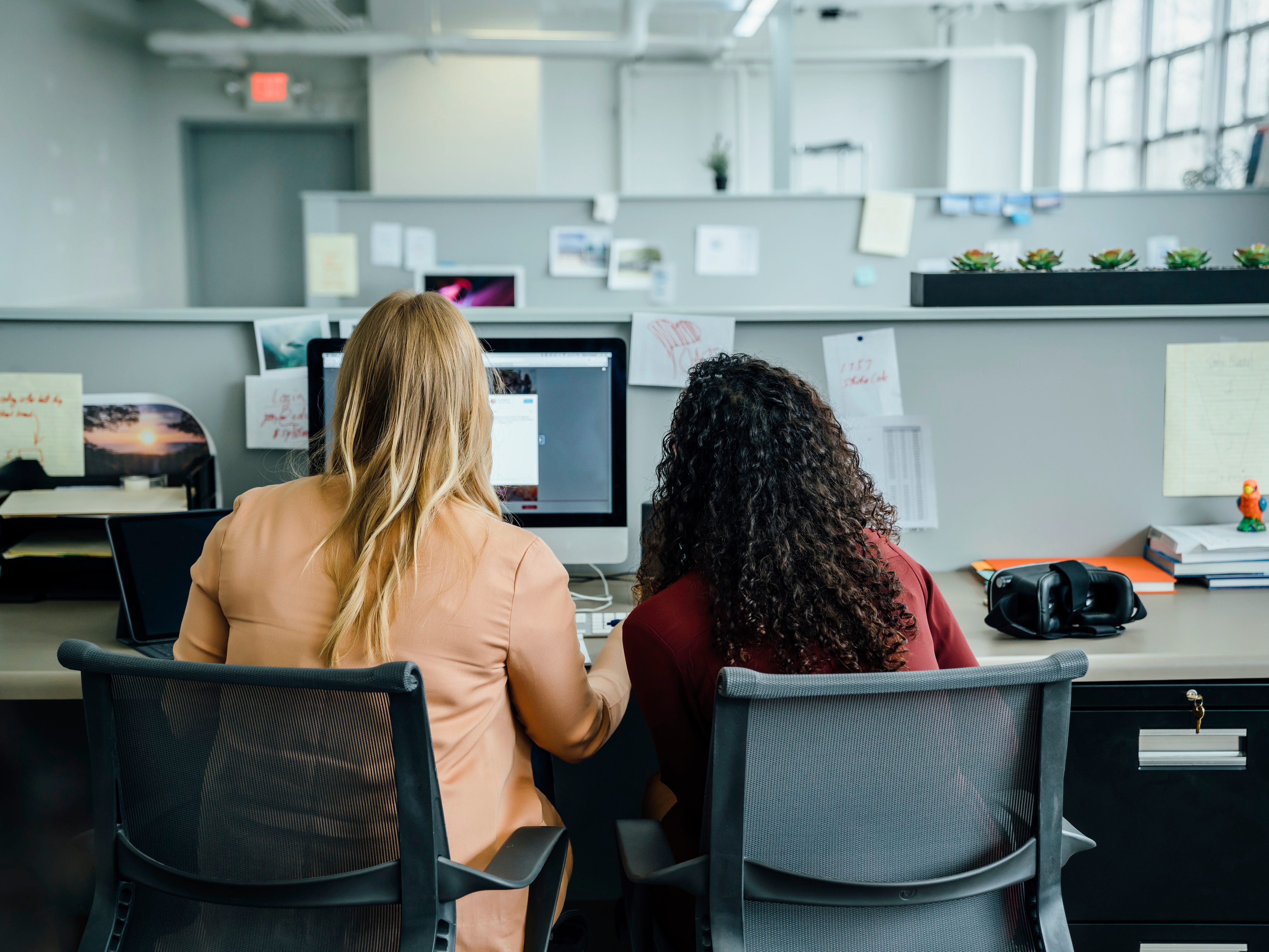 two women in the office sitting at a desk and looking at computer