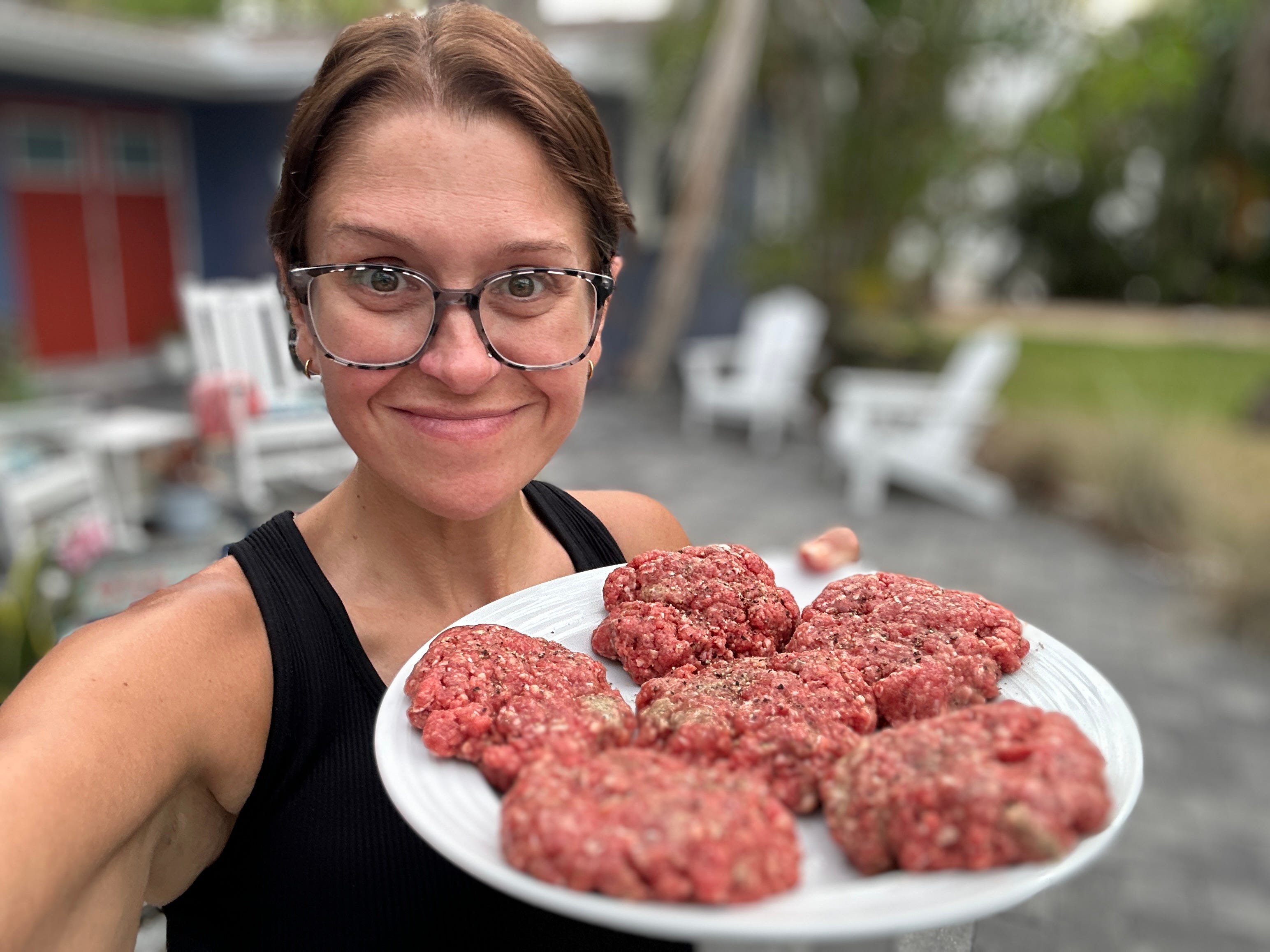 A selfie of the writer holding a plate of six raw burger patties.