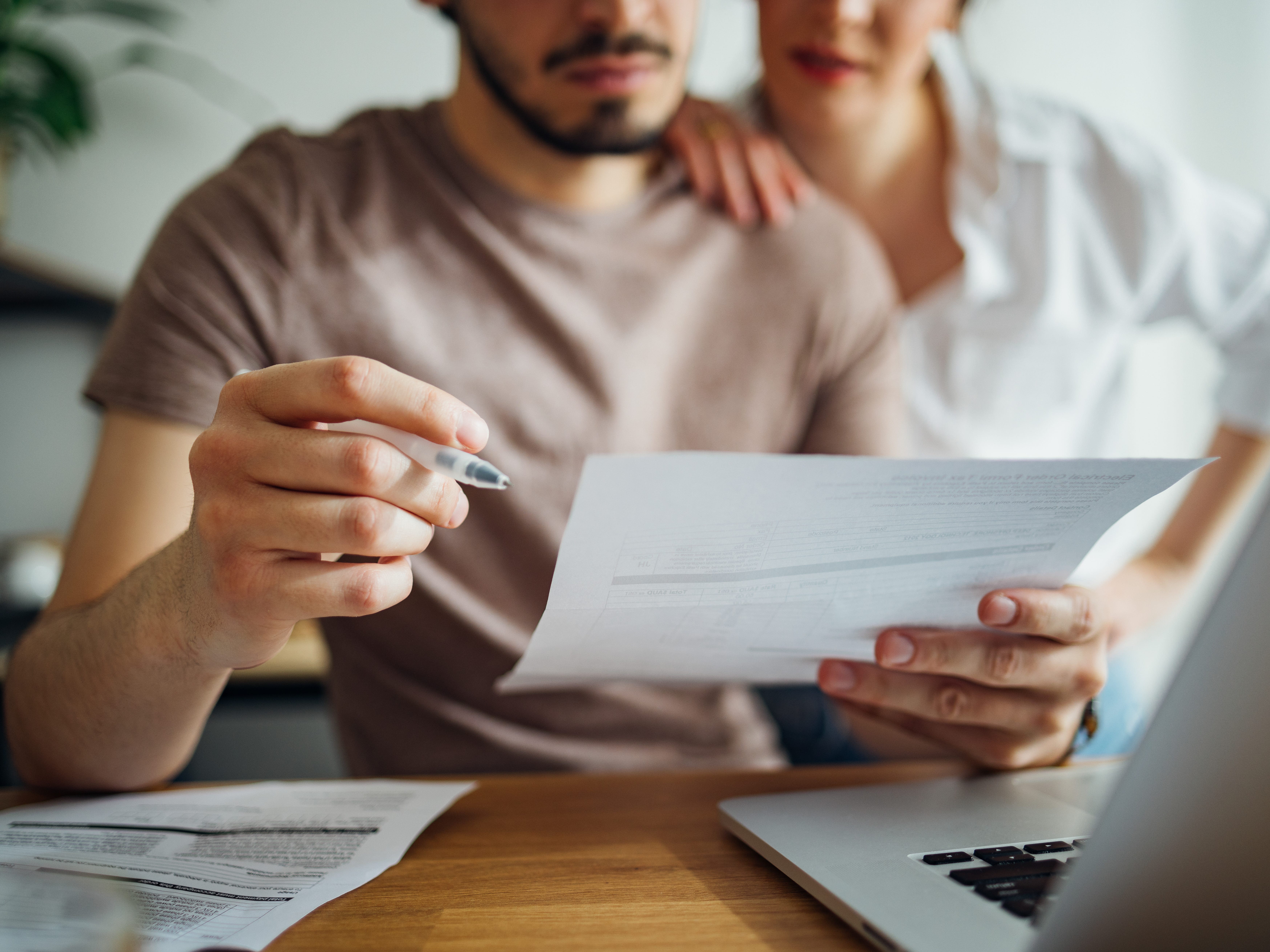 A husband and wife are talking about a bill next to a laptop; close-up picture, the couple is unrecognizable.