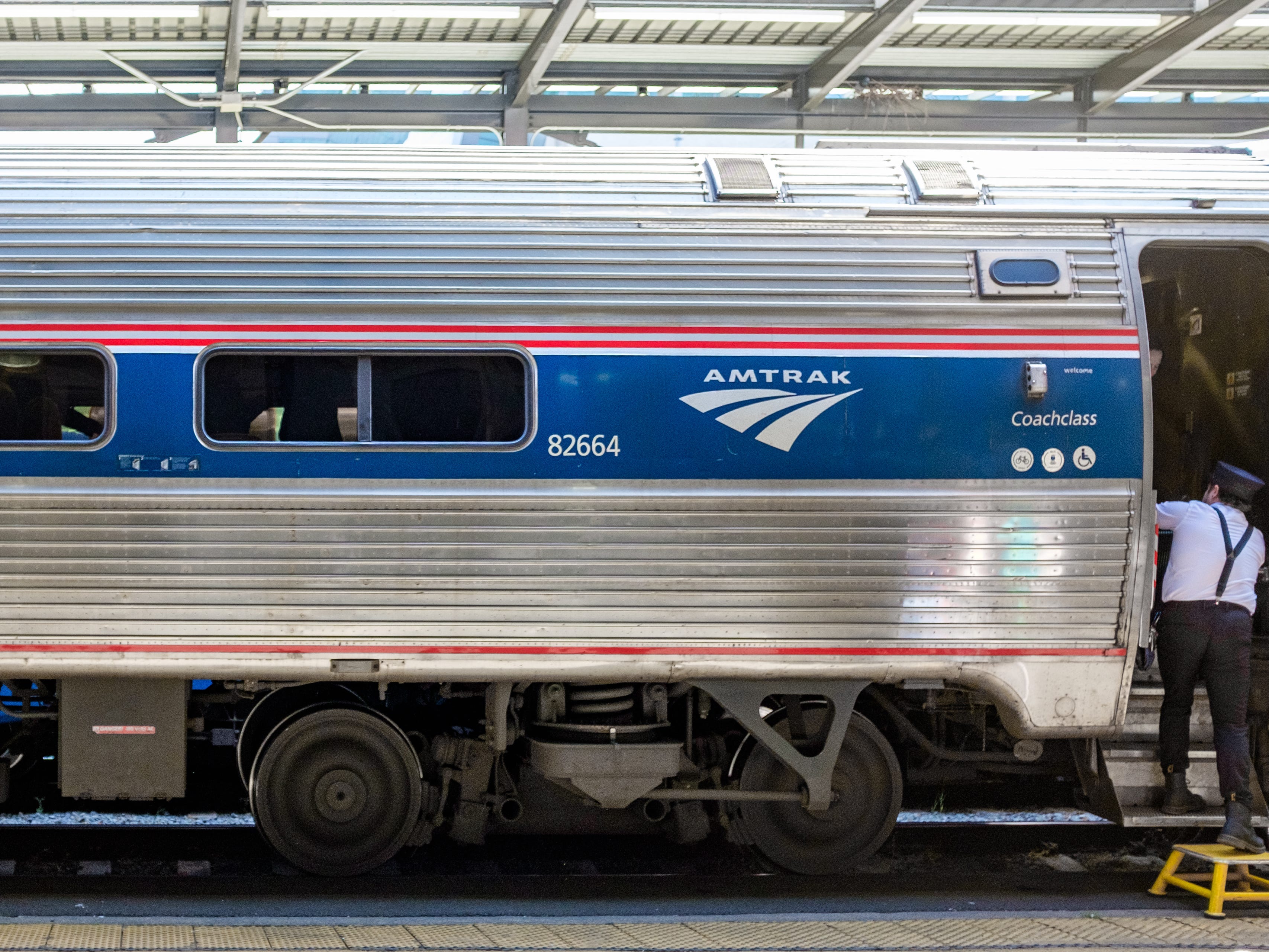 The exterior of a coach Amtrak train car with an attendant stepping out a door on the right