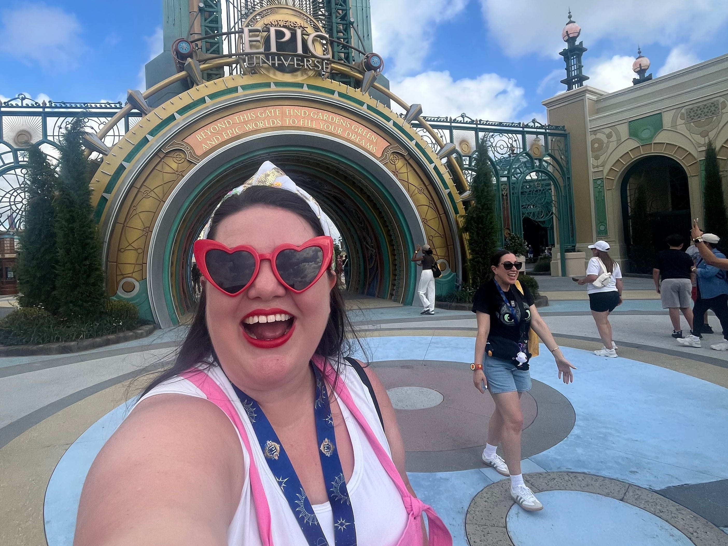 Author Megan duBois smiling while wearing heart-shaped sunglasses near entrance of Epic Universe