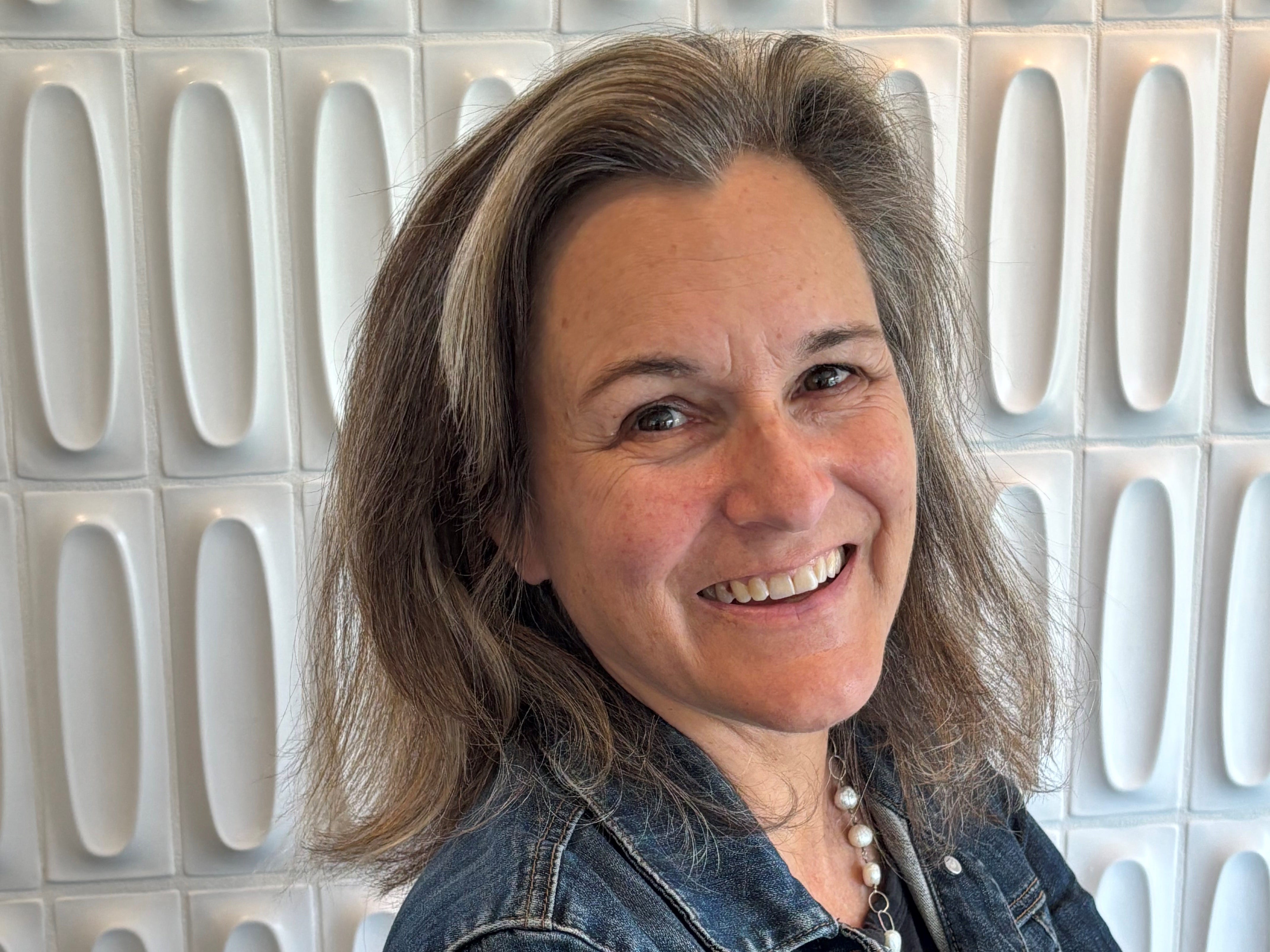 smiling woman in a denim jacket against a white tile background
