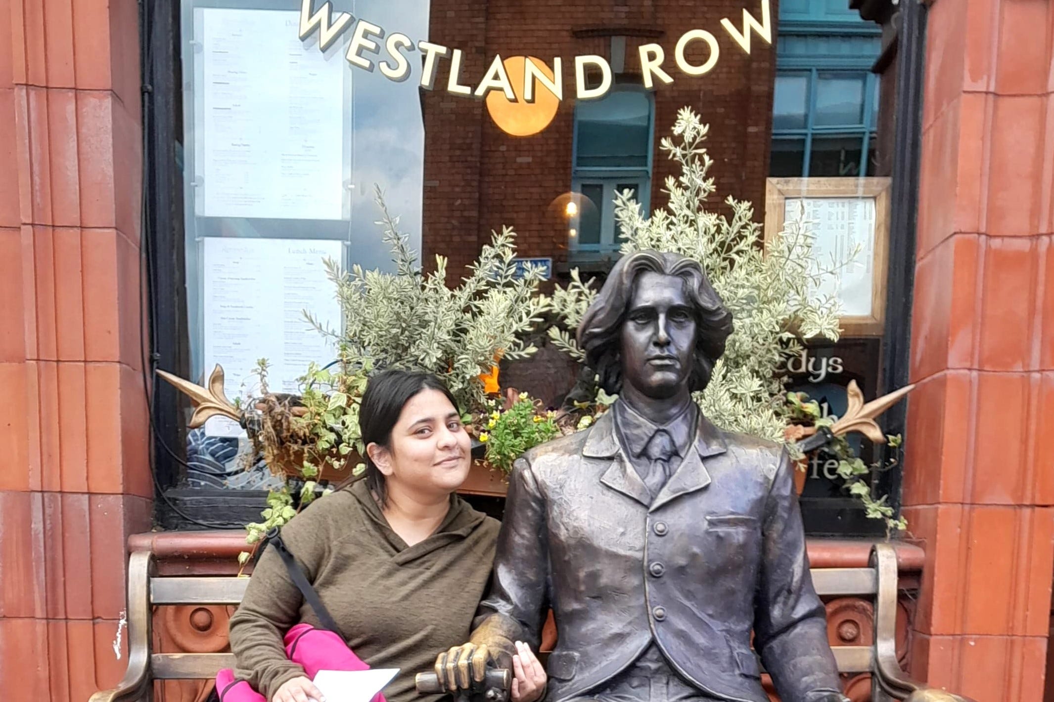 A woman sits next to a statue on a bench in Dublin, Ireland.